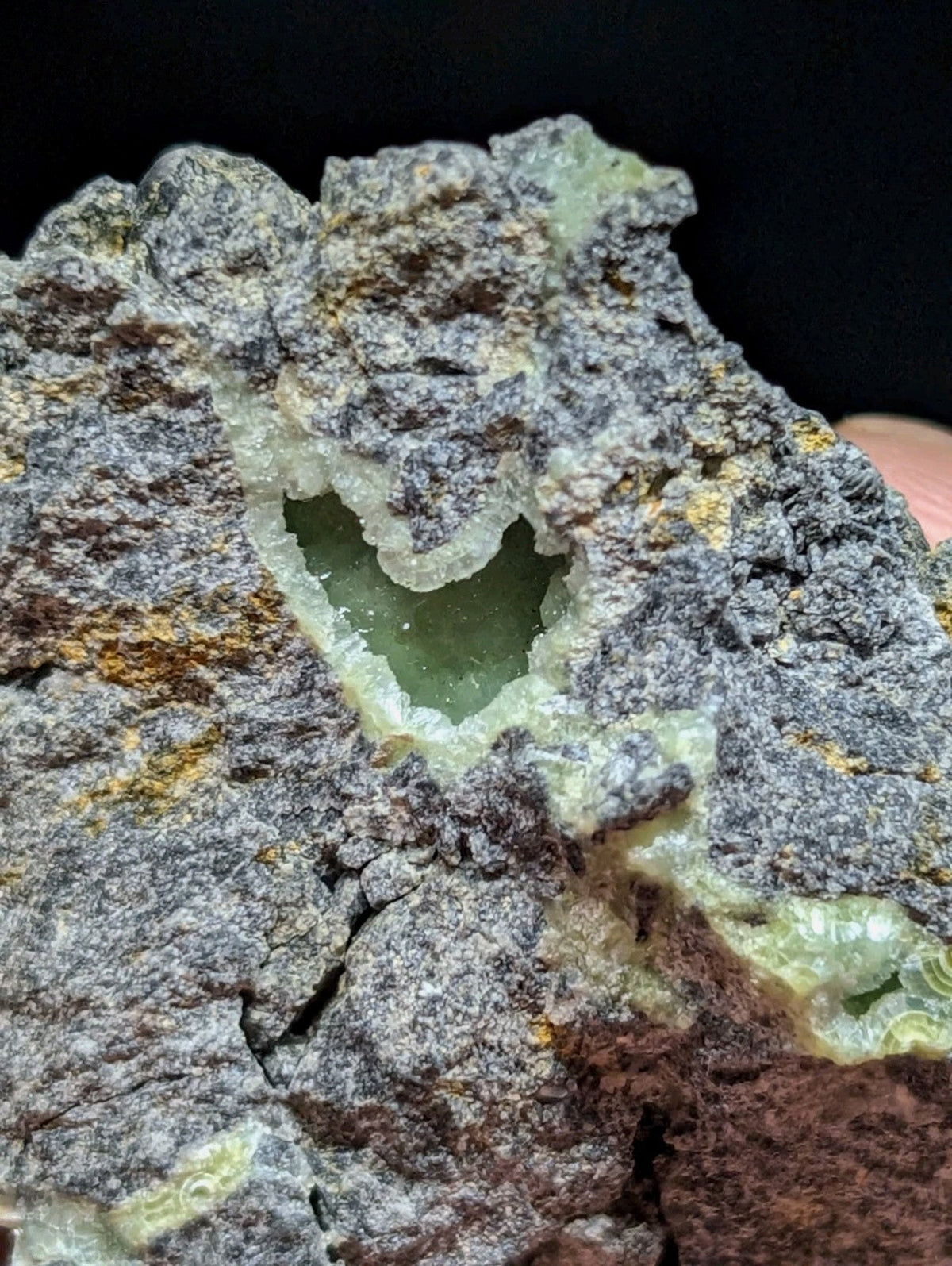 A heart-shaped cavity in a rough, grayish-green mineral specimen with translucent green crystals forming its inner walls.