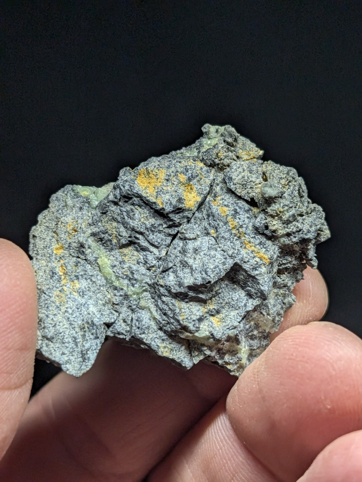 A rough, irregularly shaped rock with a grayish-green base color and patches of yellow mineral streaks.