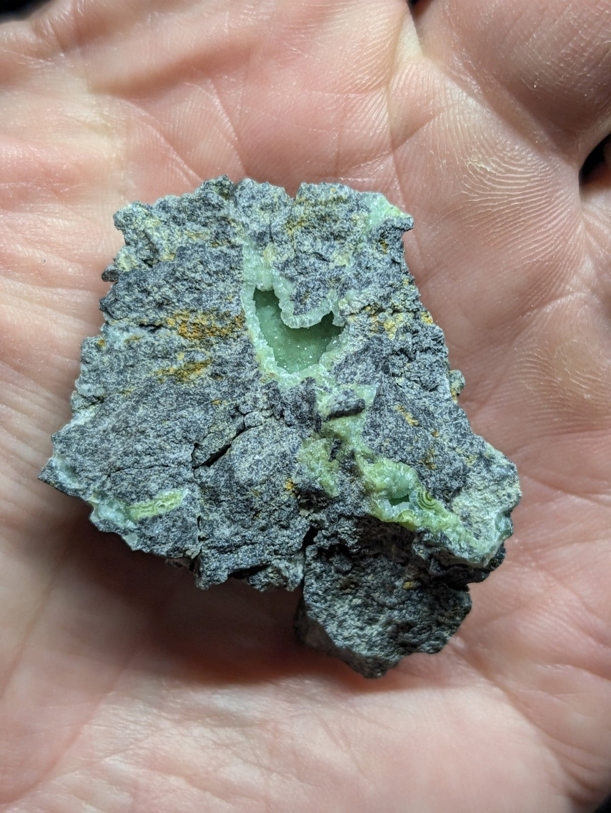 A rough, irregularly shaped mineral specimen with a grayish matrix and vibrant green crystalline formations.