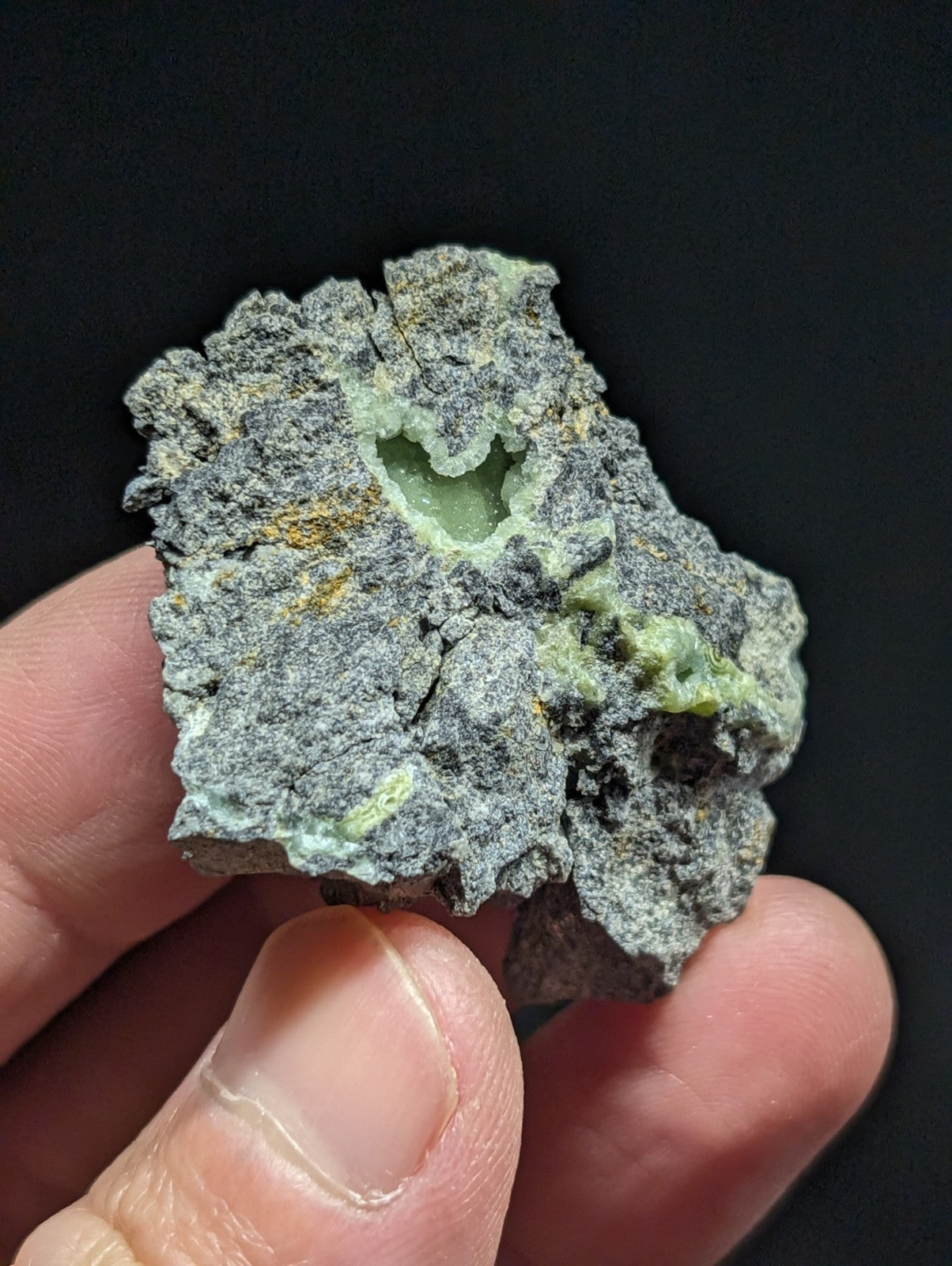 A rough, irregularly shaped mineral specimen with a gray matrix and patches of greenish-yellow crystalline material.