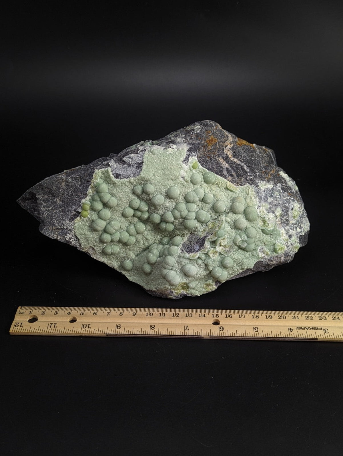 A striking greenish-gray mineral specimen featuring a cluster of rounded, bulbous formations on a dark rock base.