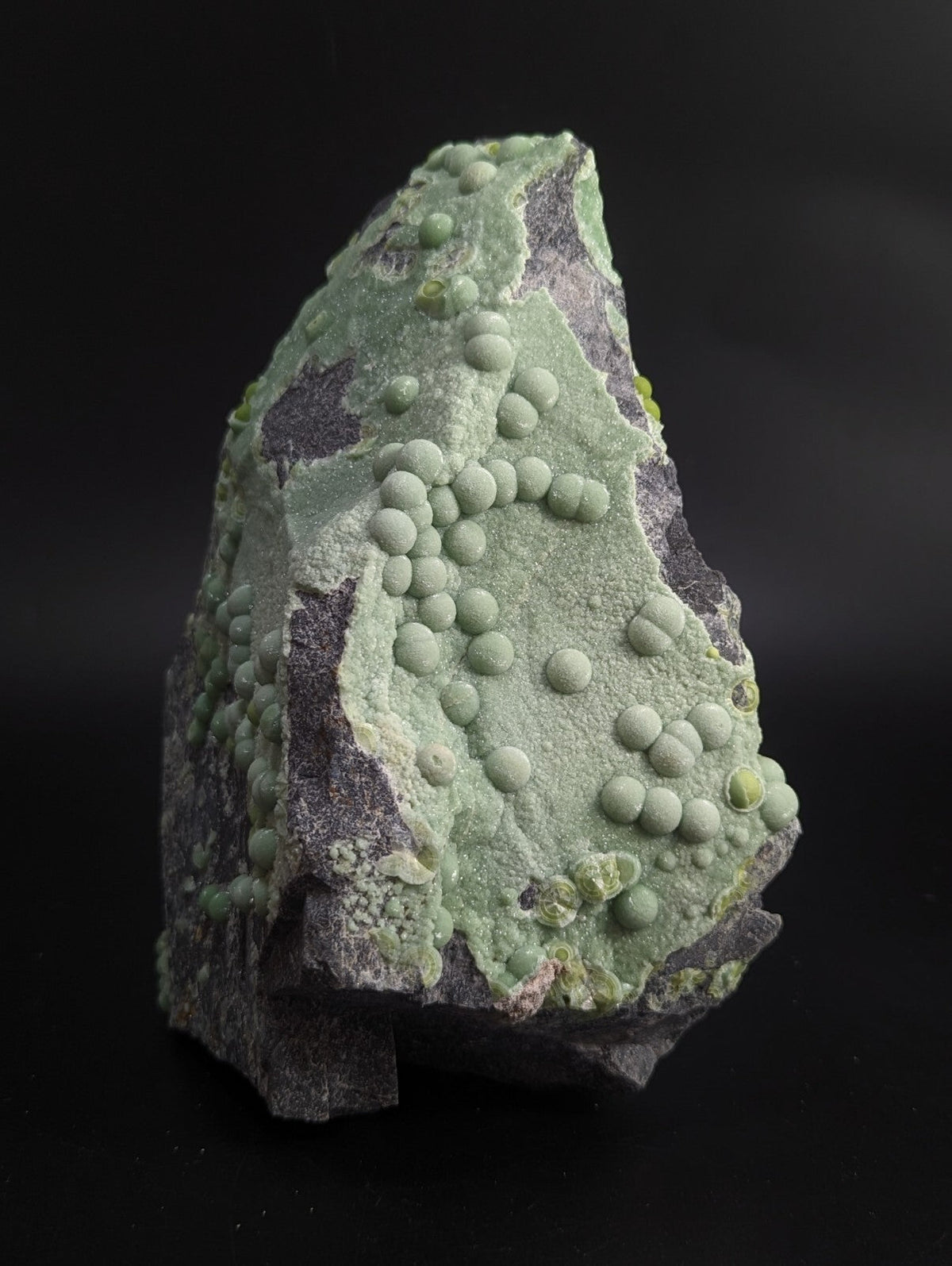 A striking green mineral specimen featuring a textured surface with numerous rounded, bulbous formations clustered across its face.