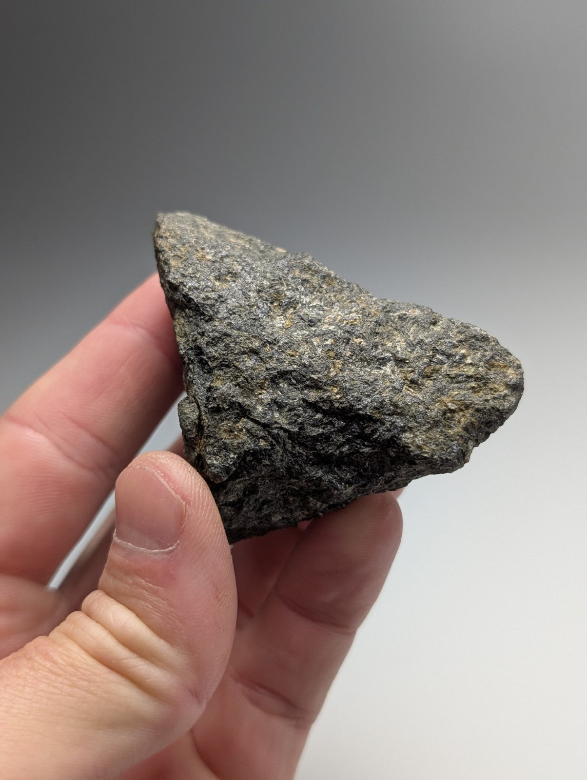 A rough dark gray jacupirangite rock with a textured surface held in hand from magnet cove hot spring county Arkansas