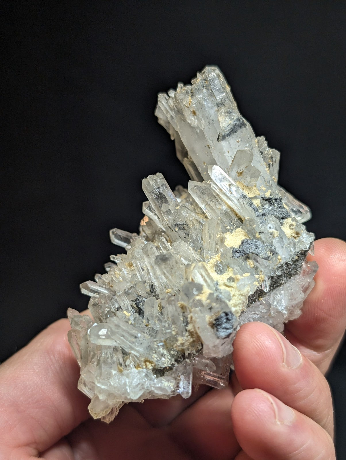 A translucent quartz crystal cluster with clear, faceted points and speckles of yellow and dark mineral inclusions.