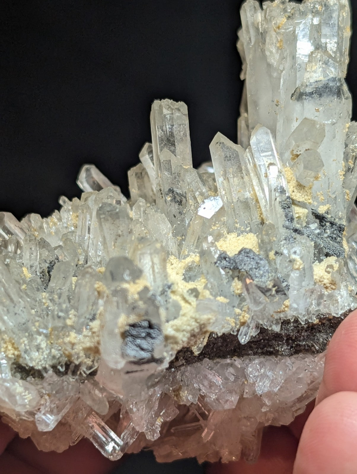 A translucent quartz crystal cluster with golden mineral inclusions and dark matrix, held by a hand.