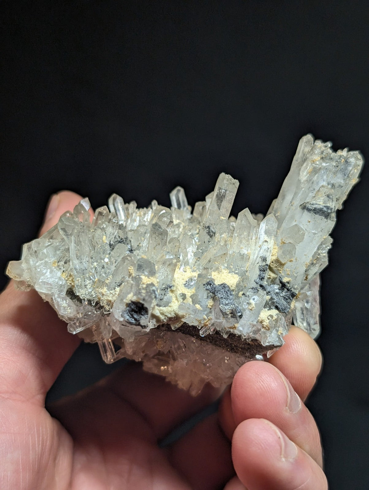 A translucent, crystalline mineral specimen with clear quartz-like crystals interspersed among dark and yellowish matrix material.