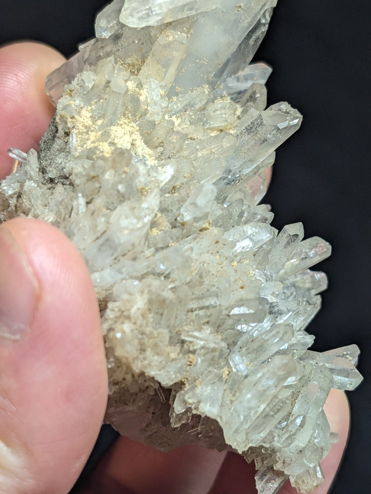 A cluster of translucent, clear quartz crystals with sharp, pointed facets and a few golden mineral inclusions.