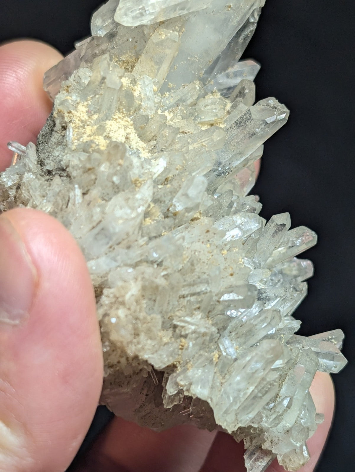 A cluster of translucent, clear quartz crystals with sharp, pointed facets and a few golden mineral inclusions.