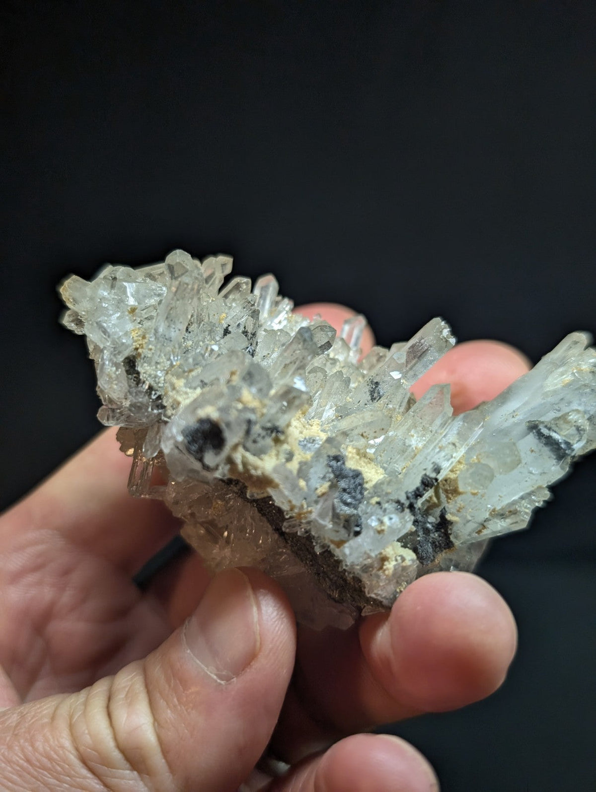 A translucent quartz crystal cluster with sharp, pointed facets and embedded dark mineral inclusions.