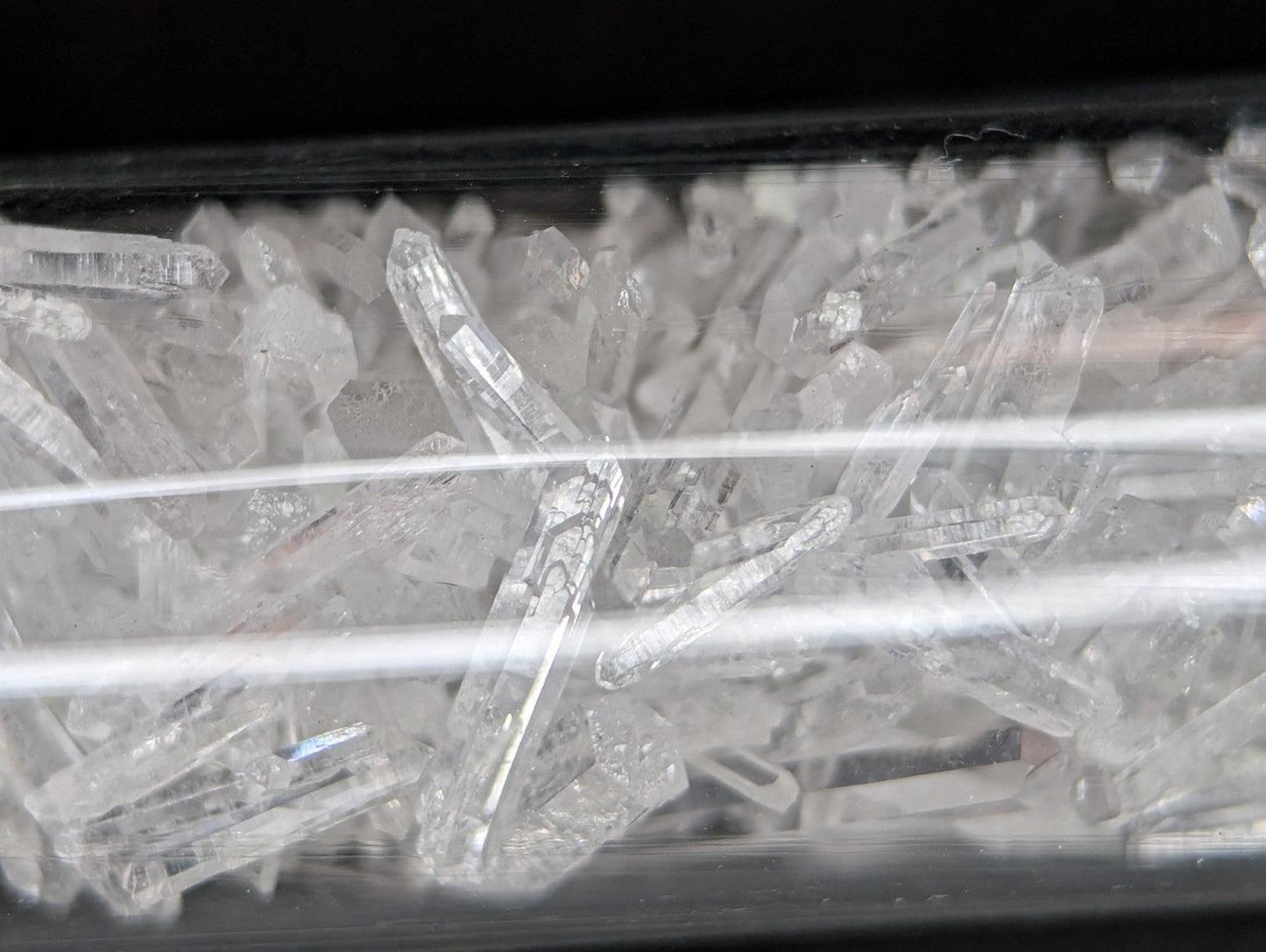 Clear quartz crystals with pointed tips and faceted surfaces, displayed in a transparent container.