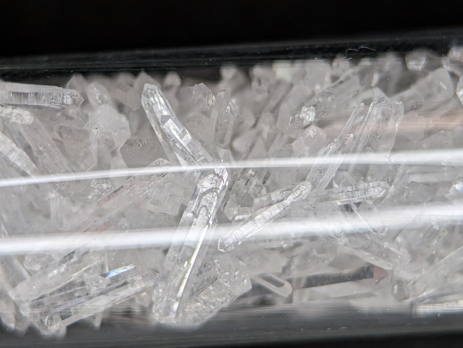 Clear quartz crystals with pointed tips and faceted surfaces, displayed in a transparent container.