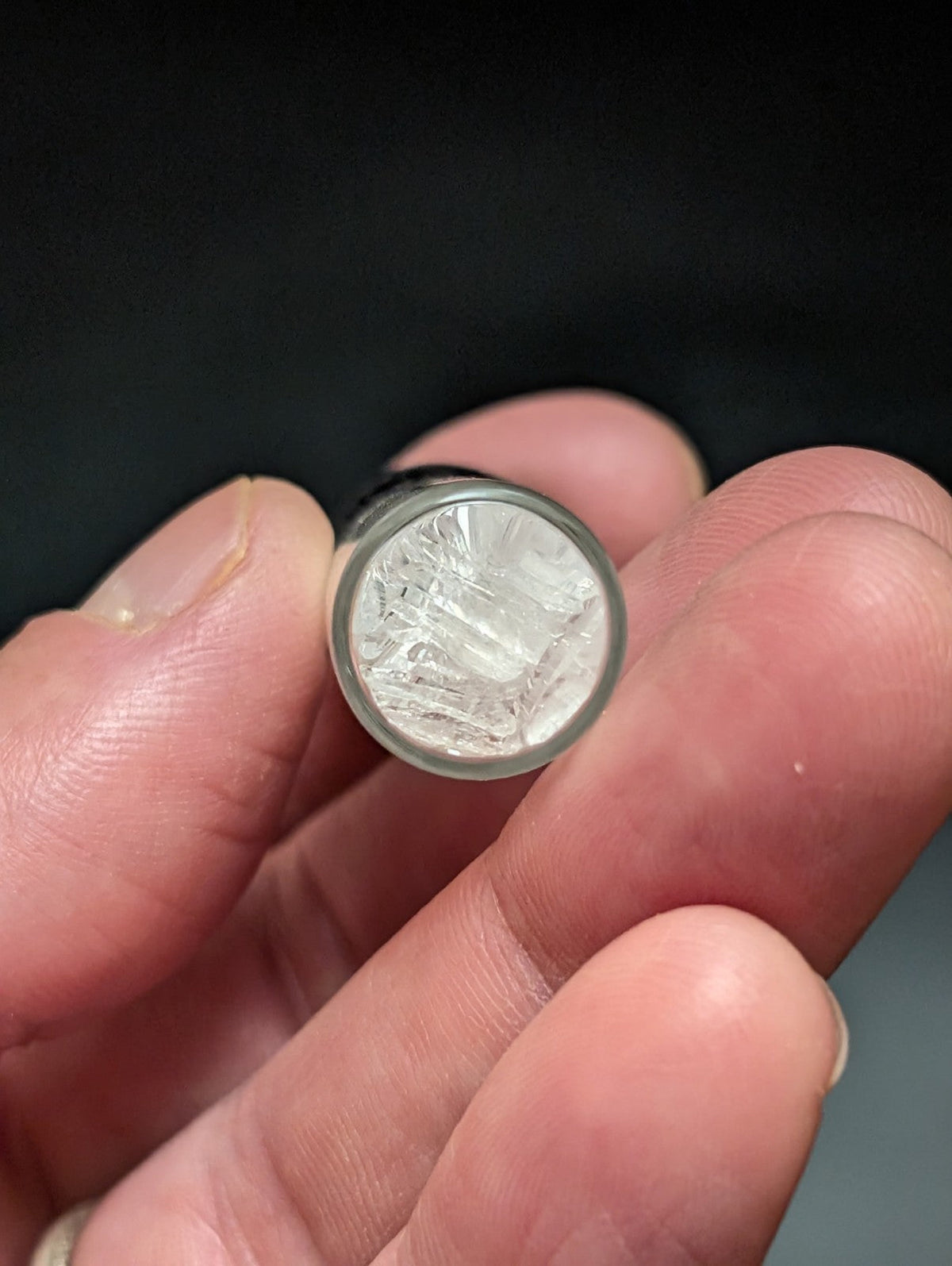A clear, cylindrical glass vial with a metallic silver rim and an intricate internal crystalline structure.