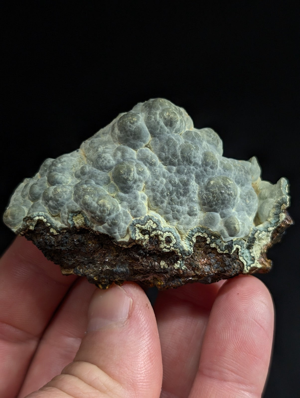 A textured, light gray and white mineral specimen with a bumpy surface held in hand.
