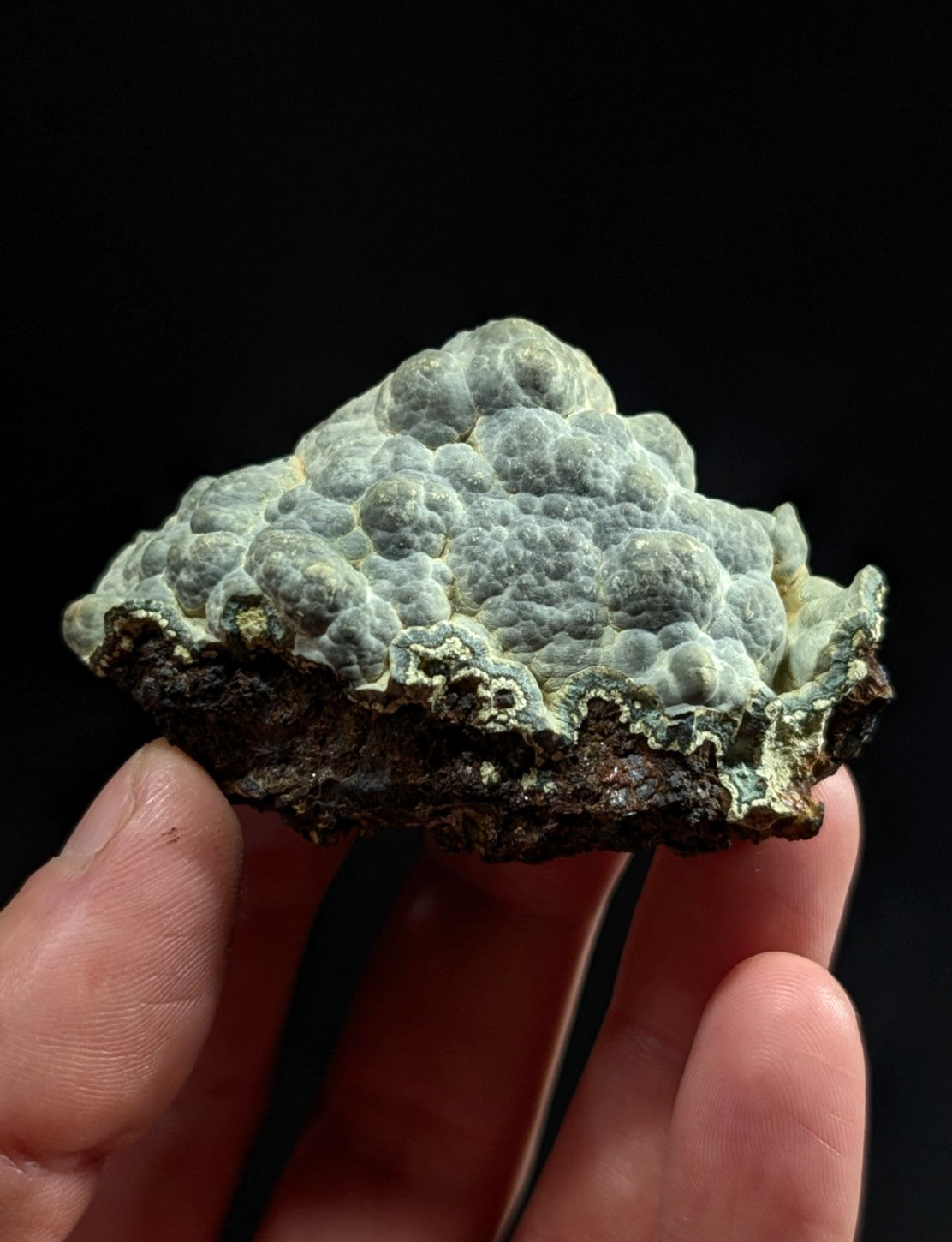 A textured, light greenish-gray mineral specimen with a bumpy, cauliflower-like surface and darker, rougher base.
