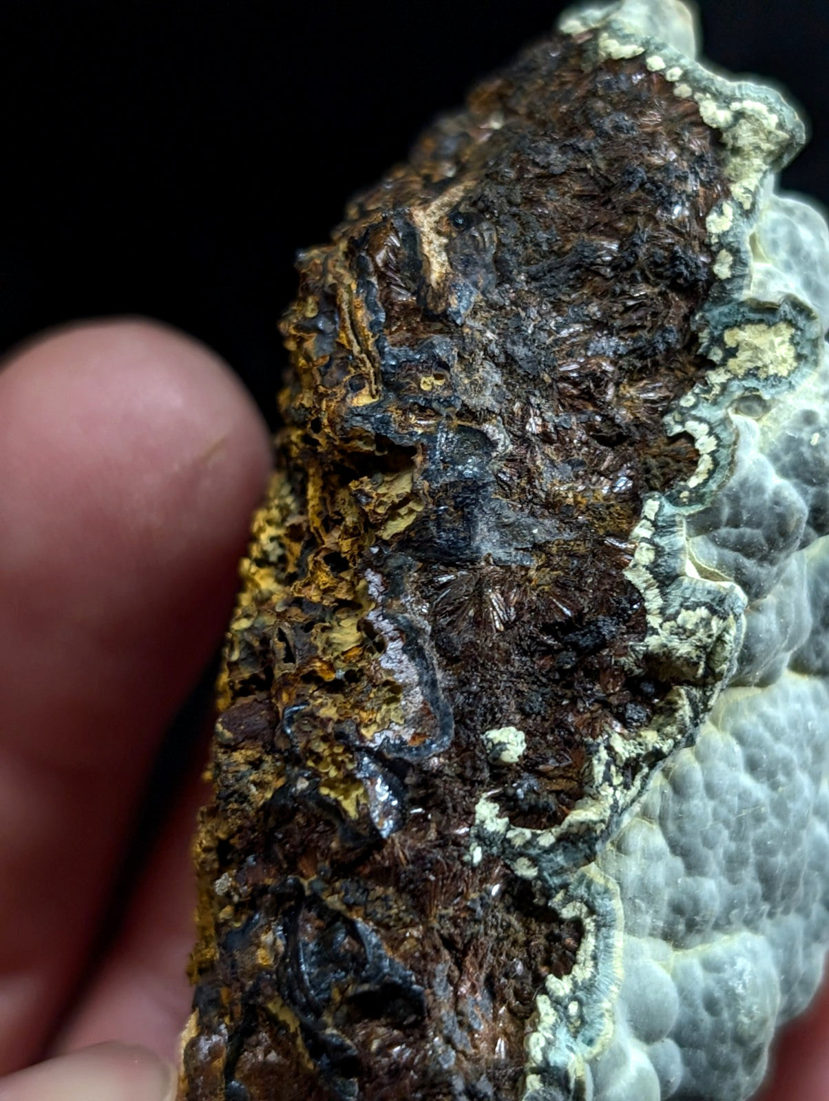 A rugged, naturally occurring mineral specimen with a textured surface featuring patches of dark brown and black minerals interspersed with lighter greenish-white crystalline formations.