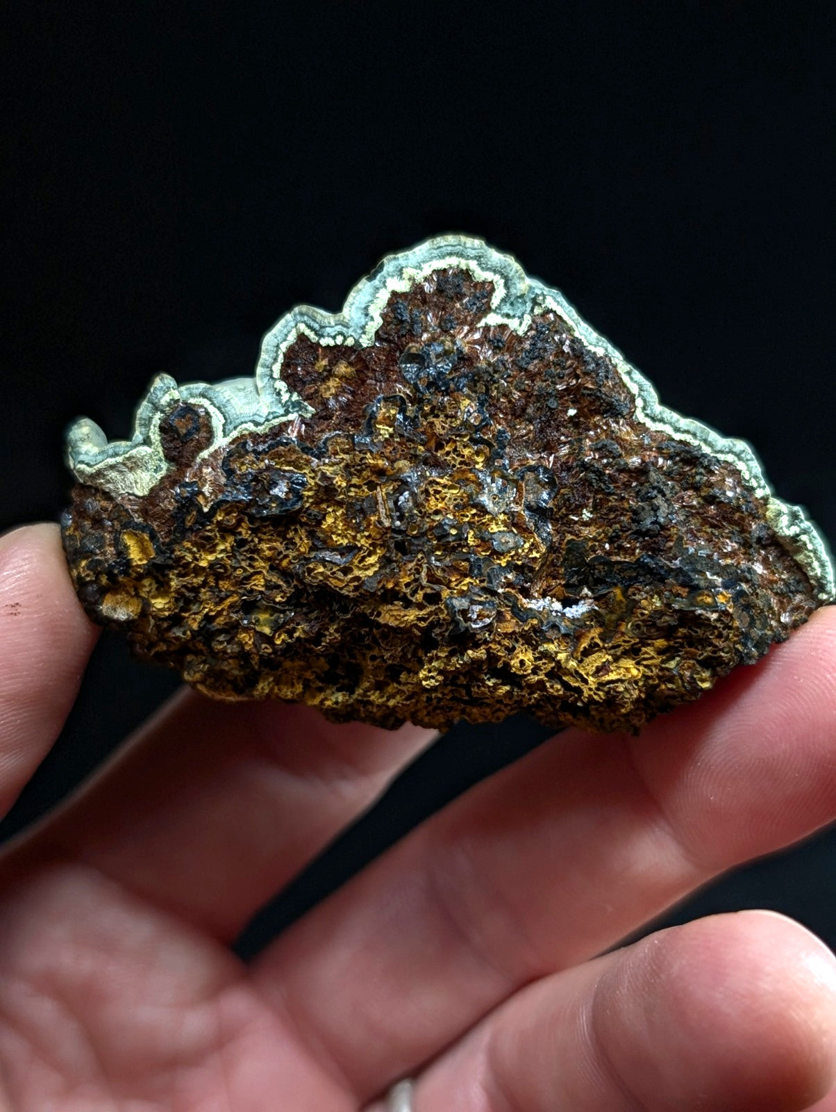 A rugged, irregularly shaped mineral specimen with a textured surface displaying patches of earthy brown and golden hues bordered by a distinct greenish patina.