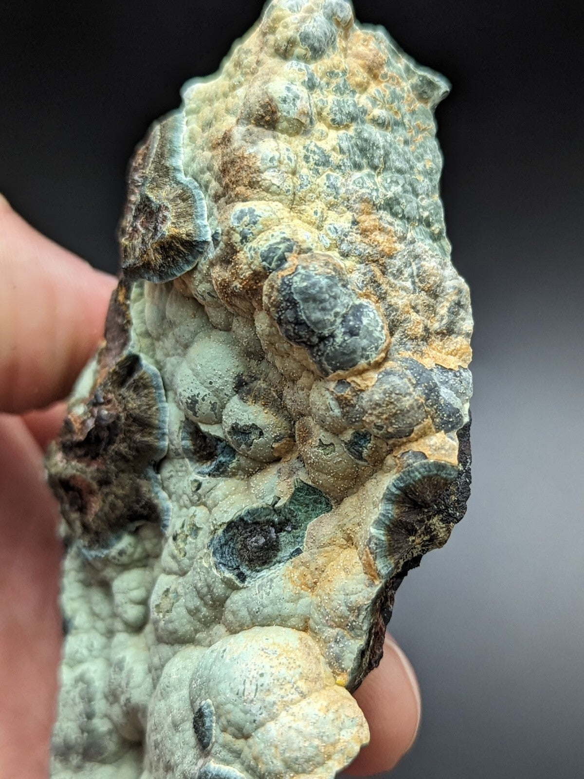 A textured, irregularly shaped mineral specimen with a mottled surface of greenish-blue, gray, and yellowish-brown hues.