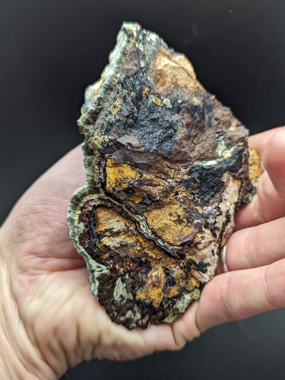 A rugged, irregularly shaped mineral specimen with a textured surface displaying patches of earthy brown, vibrant yellow, and dark grayish-black hues.