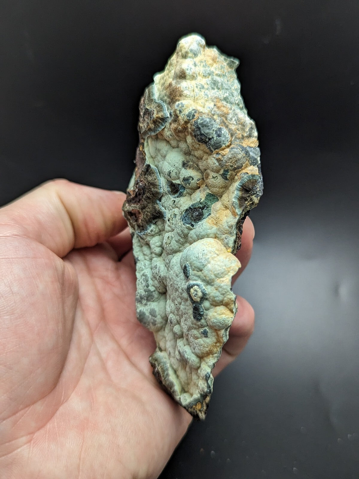 A rugged, irregularly shaped mineral specimen with a textured surface featuring patches of greenish-blue and brown hues.