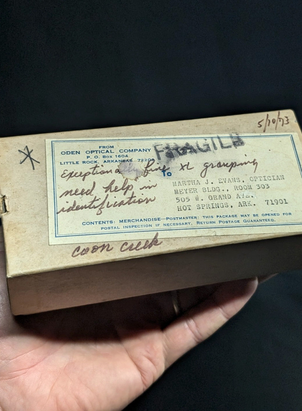 A beige cardboard box with a printed label from oden optical company, featuring handwritten notes and the word ’fragile’ in bold.