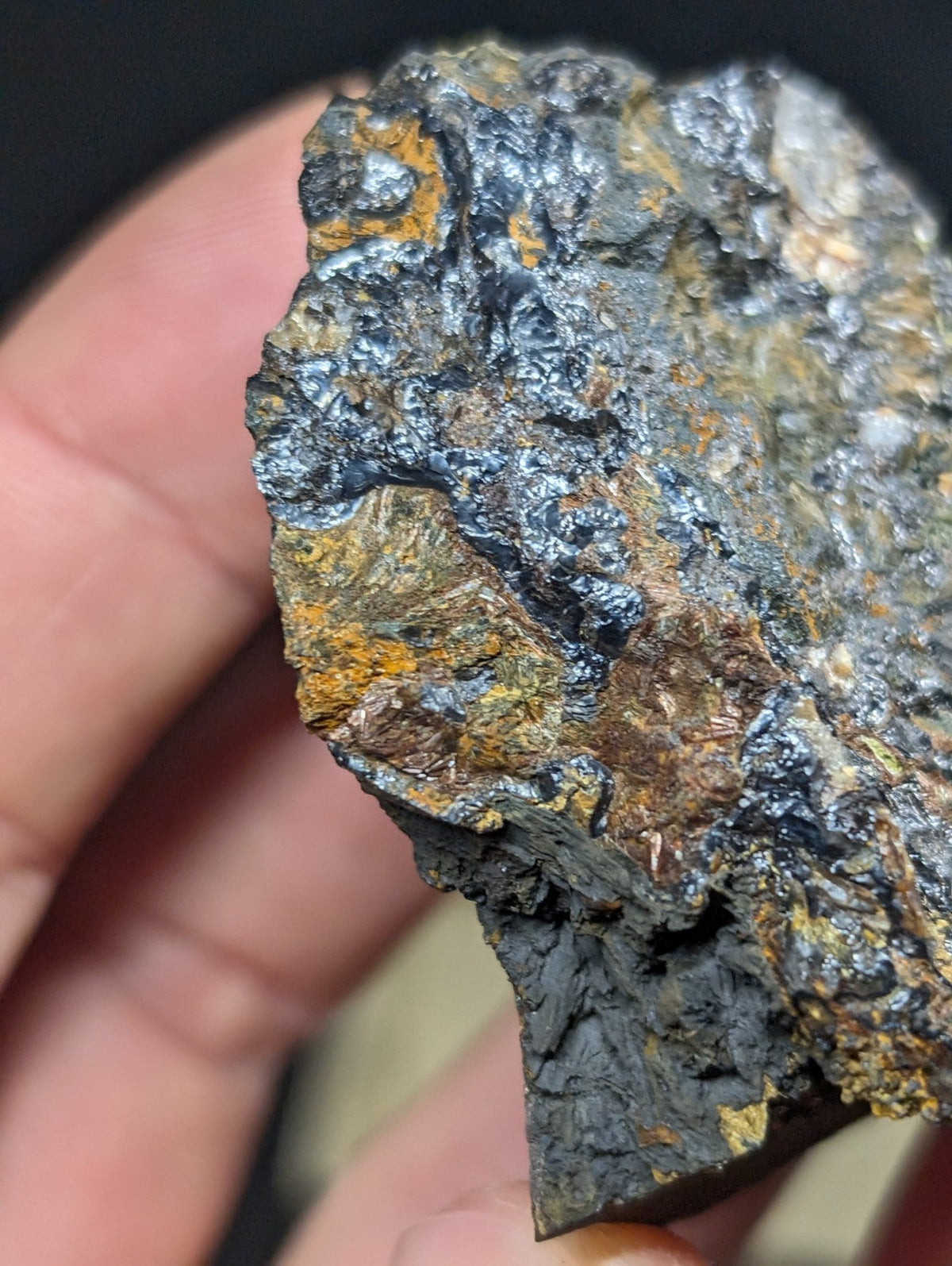 A rugged, irregularly shaped mineral specimen with a dark metallic sheen and patches of vibrant orange-yellow oxidation.