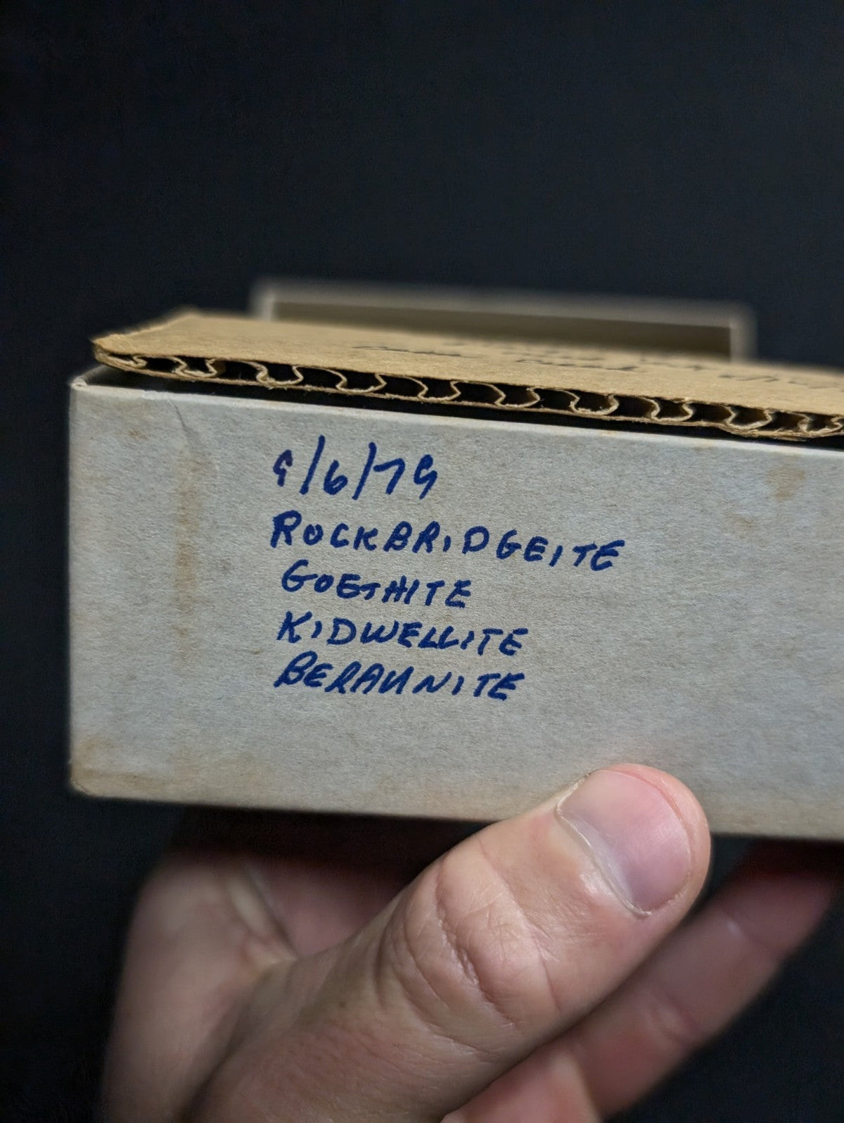 A beige cardboard box with handwritten mineral labels in blue ink.