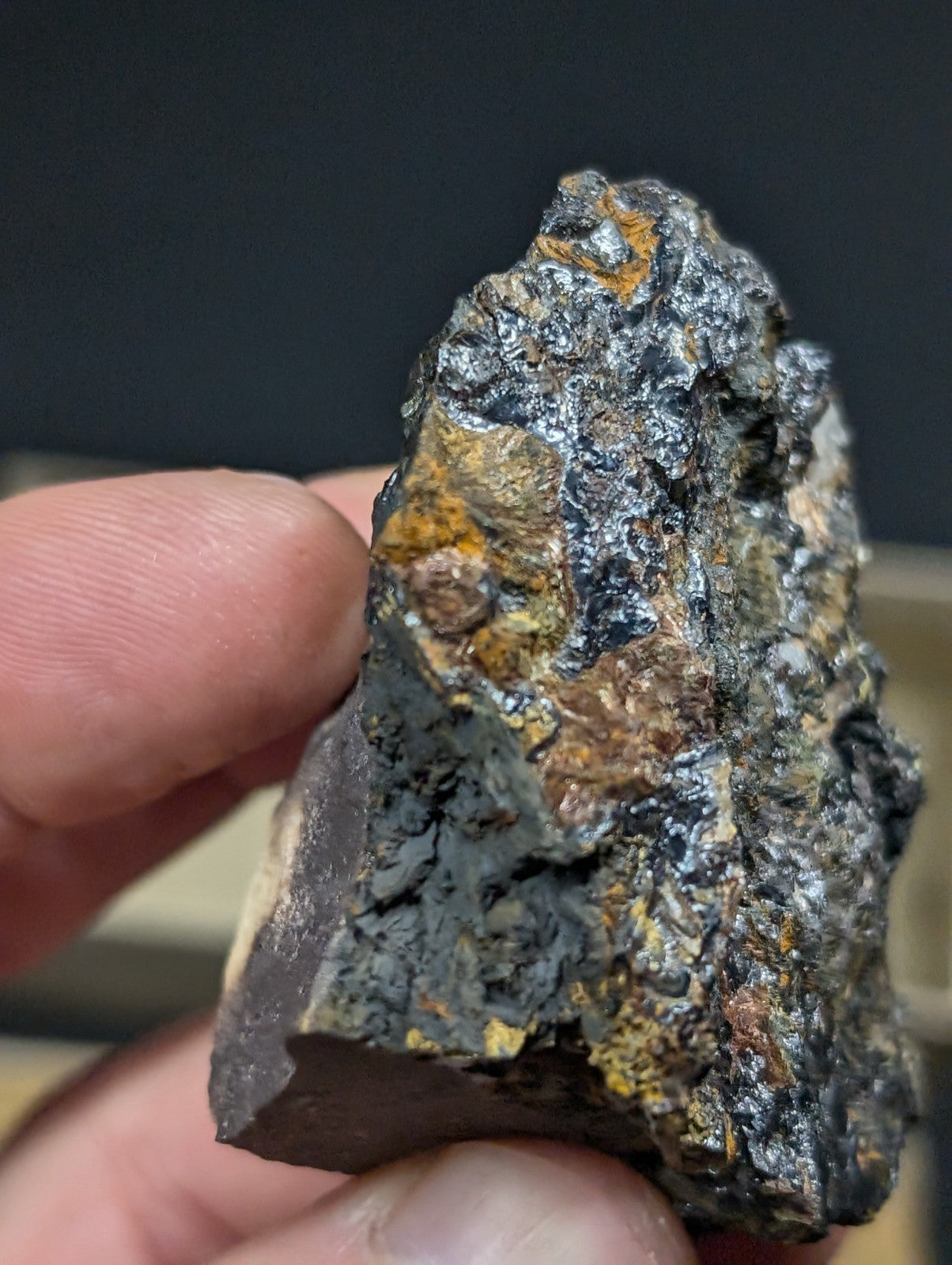 A rugged, irregularly shaped mineral specimen with a dark metallic base and patches of vibrant yellow-orange oxidation.