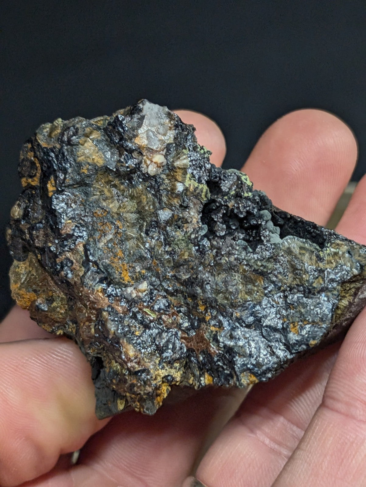 A rugged, irregularly shaped mineral specimen with a dark gray and black surface accented by patches of yellowish-orange oxidation.