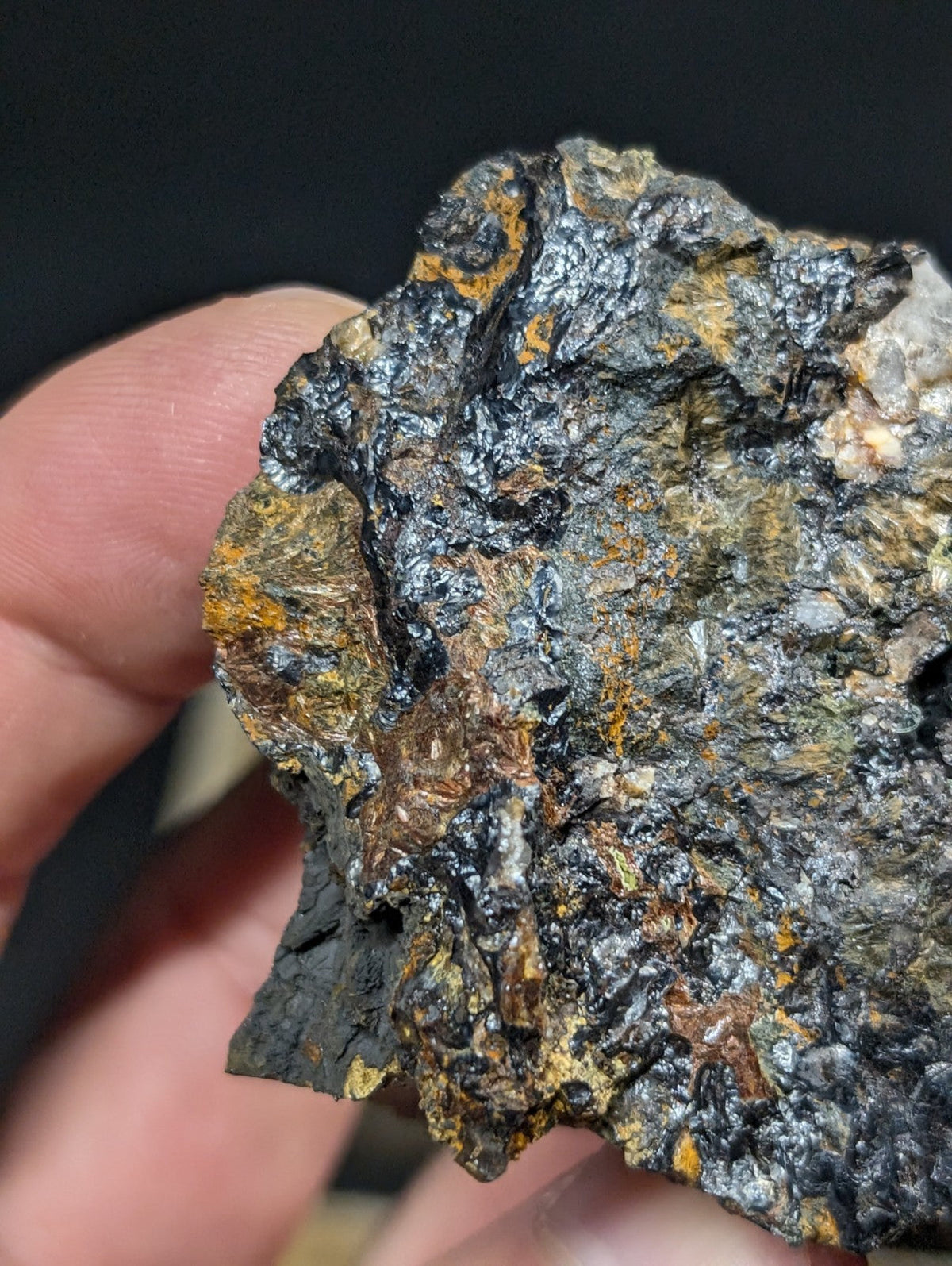 A rugged, irregularly shaped rock with a dark, metallic sheen and patches of orange-brown mineral streaks.