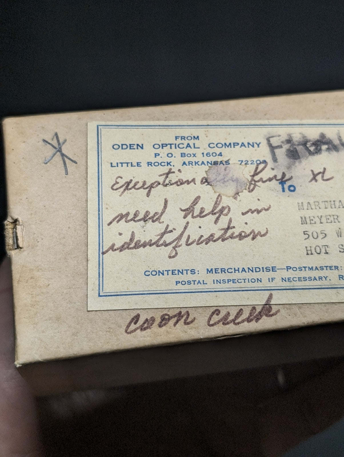 A vintage beige cardboard box with a faded blue-bordered label from oden optical company, featuring handwritten shipping details and the words ’exception fine’ in cursive script.
