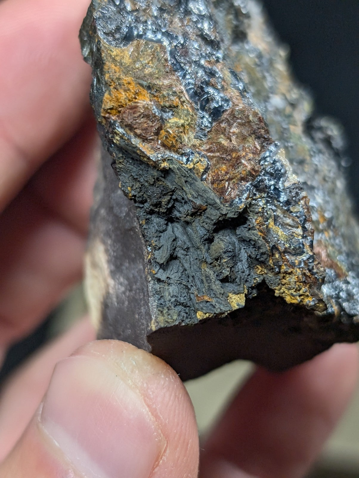 A rugged, irregularly shaped rock with a dark gray base and patches of vibrant orange-yellow mineral veins.