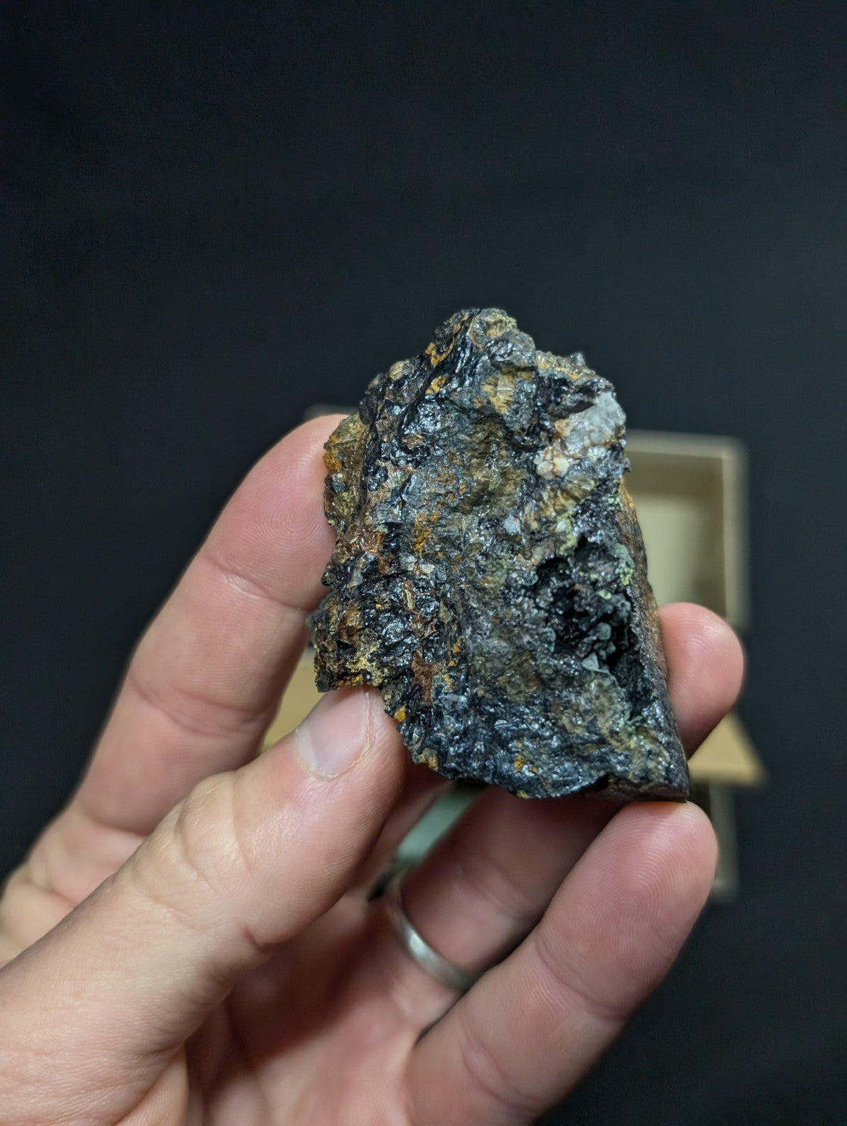 A rugged, irregularly shaped rock with a dark gray and black surface accented by patches of orange and yellow mineral streaks.