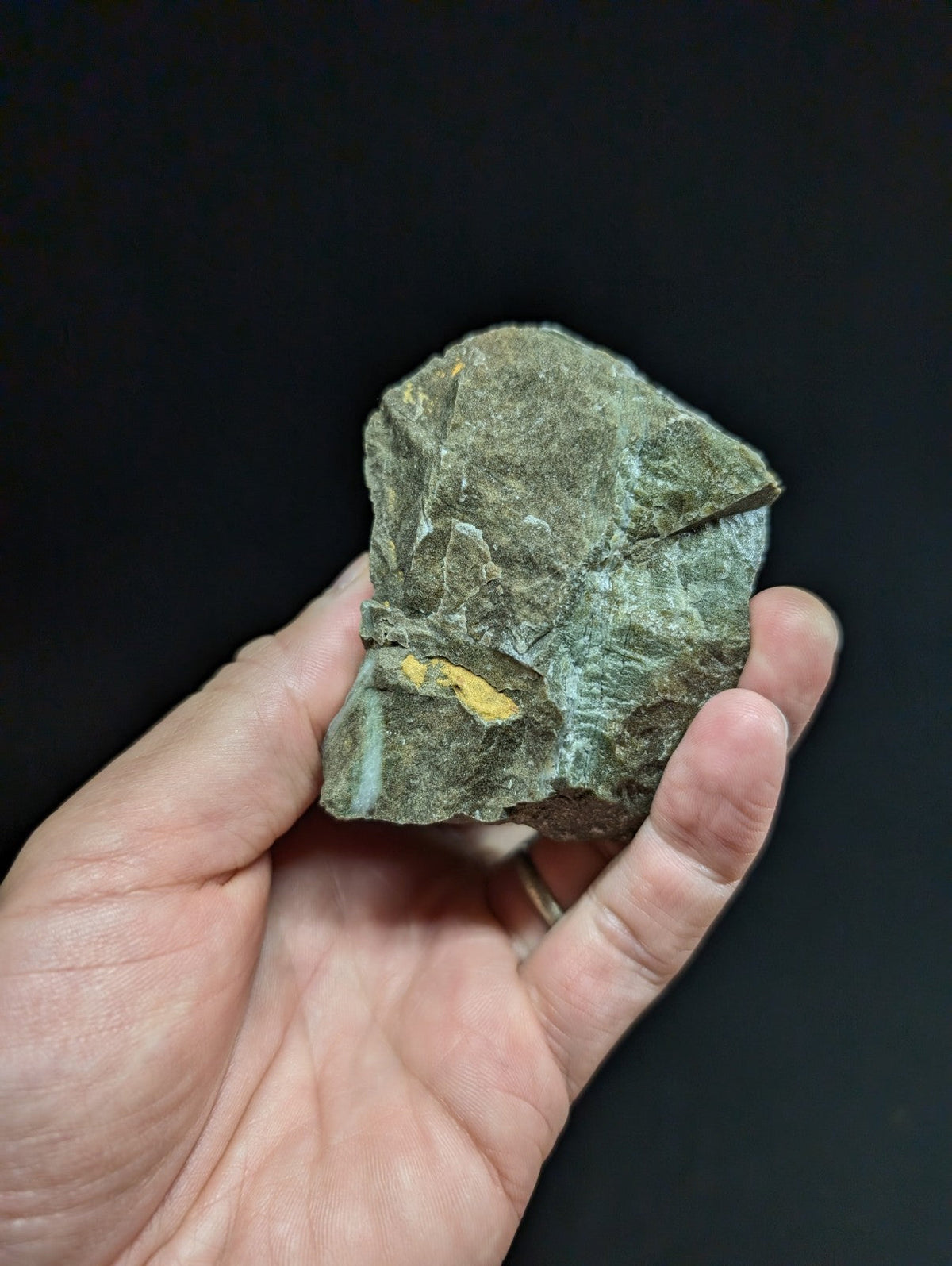 A rough, irregularly shaped greenish-gray rock with a distinct yellow streak and subtle blue-green patina.