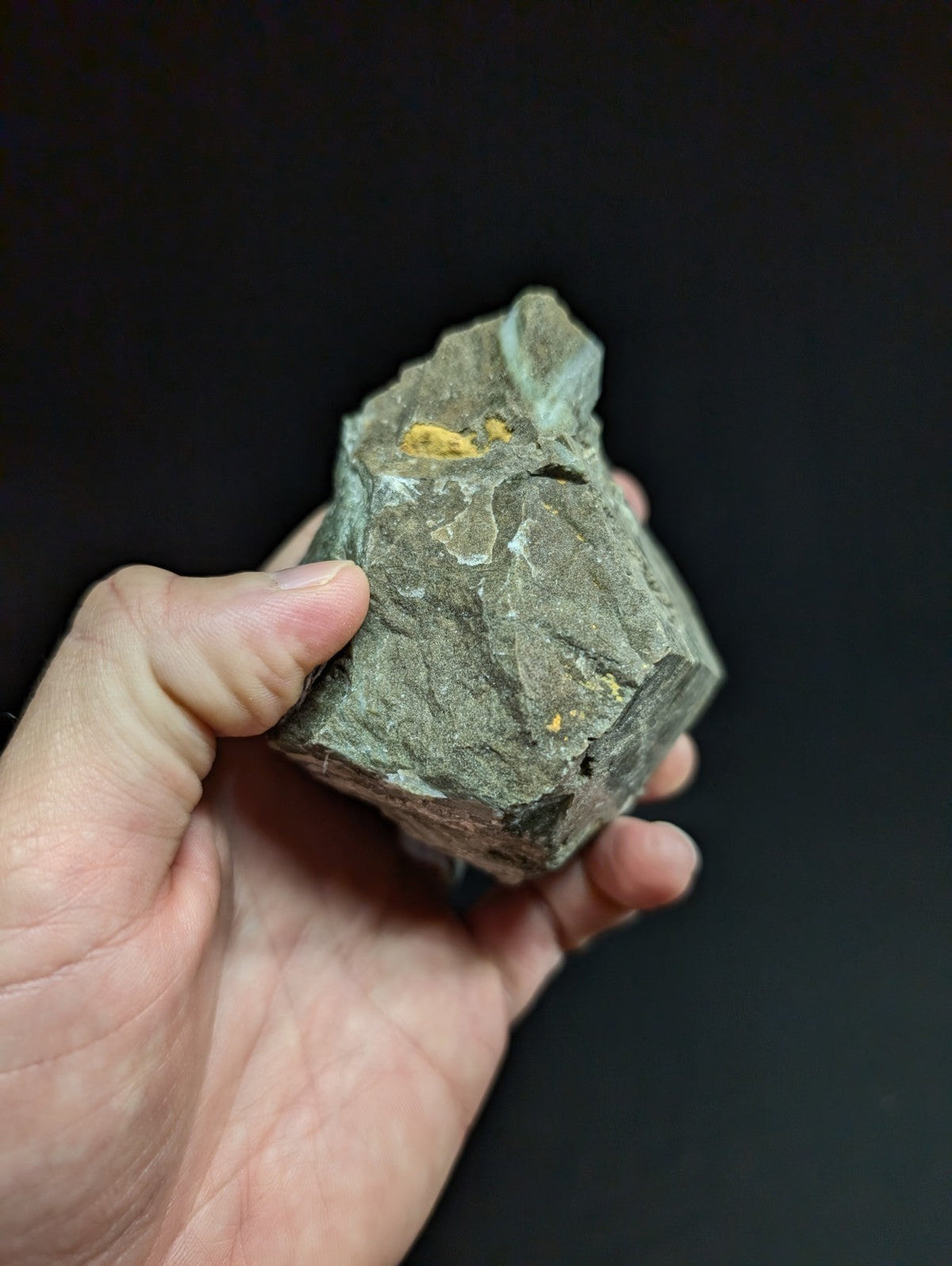 A rough, irregularly shaped gray rock with small patches of yellow mineral inclusions.