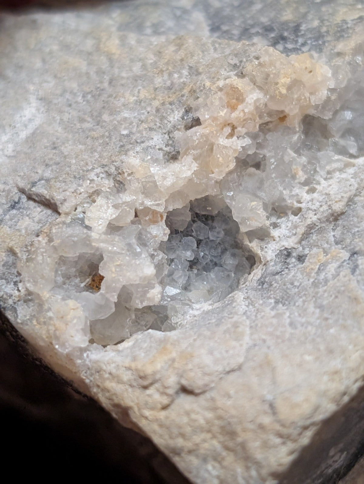 A translucent, crystalline geode with a rough gray matrix and delicate white to pale yellow mineral formations.