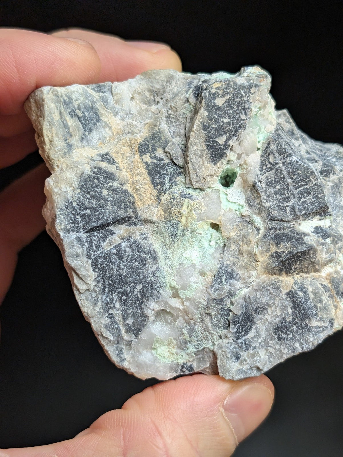 A rugged, irregularly shaped mineral specimen with a mottled gray and white surface accented by patches of pale green.