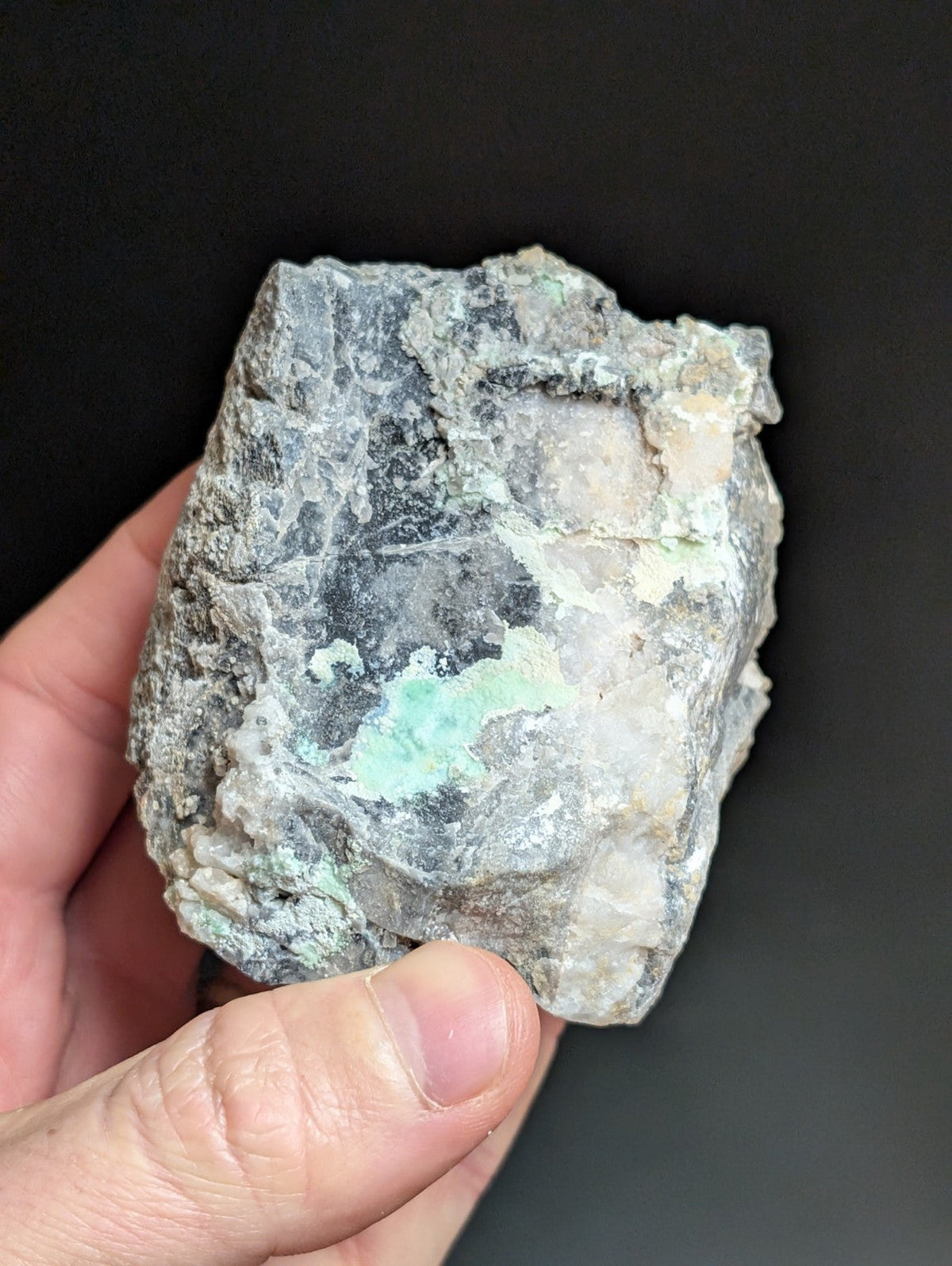 A rough, irregularly shaped mineral specimen with a mottled gray and white surface accented by patches of vibrant green.