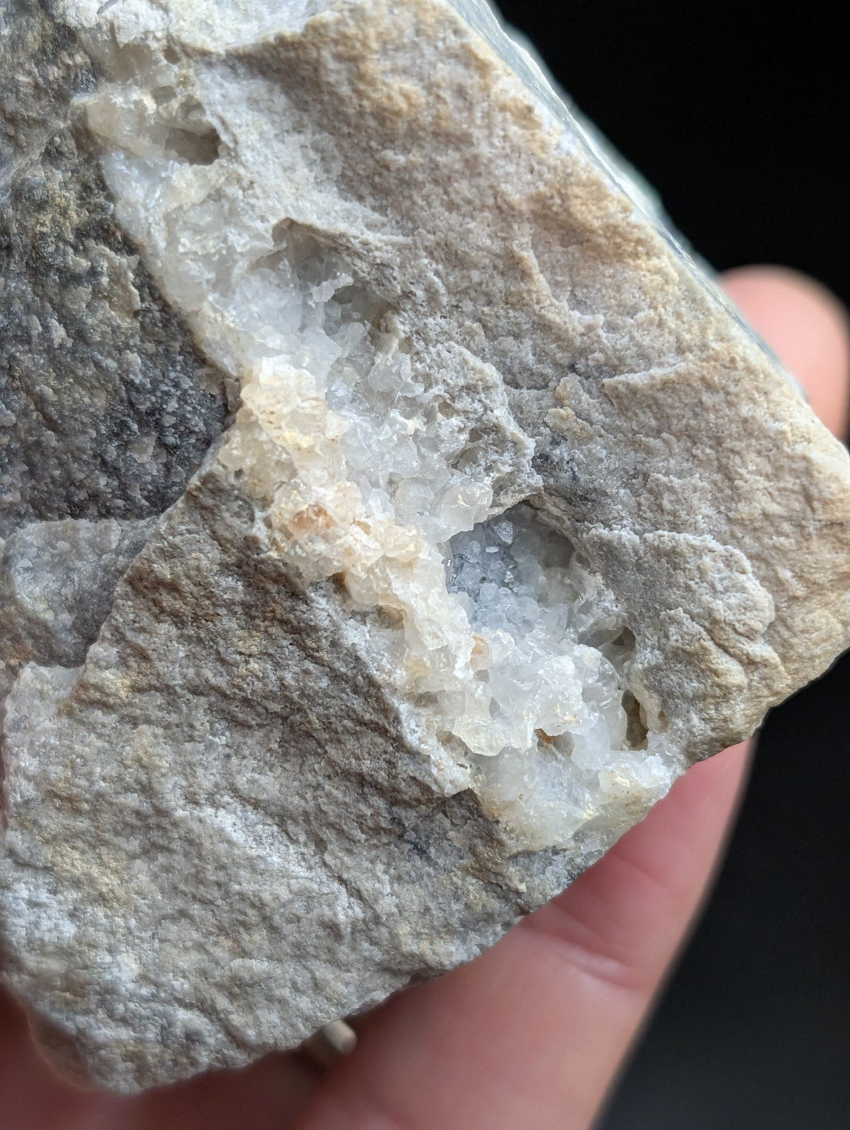 A gray rock with a crystalline interior featuring translucent white and pale blue mineral formations.