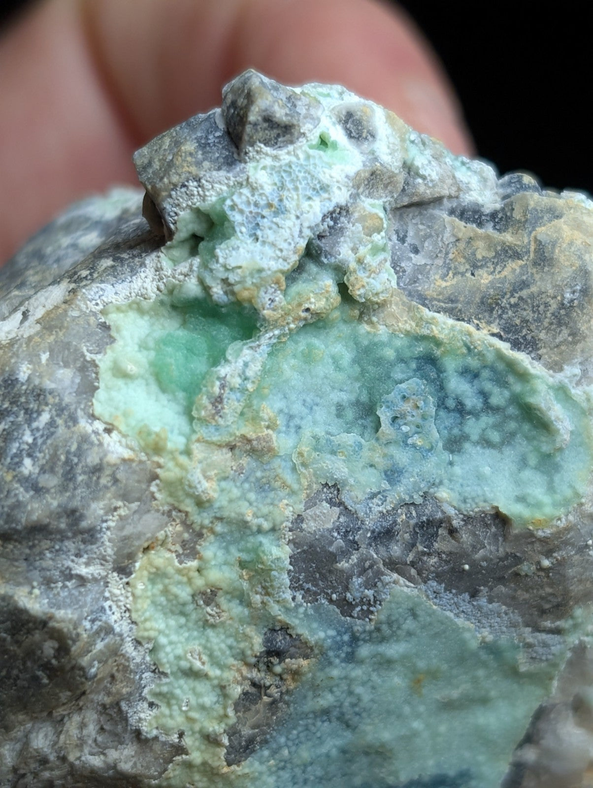 A rough, irregularly shaped mineral specimen featuring patches of vibrant green and pale blue-green hues over a grayish matrix.