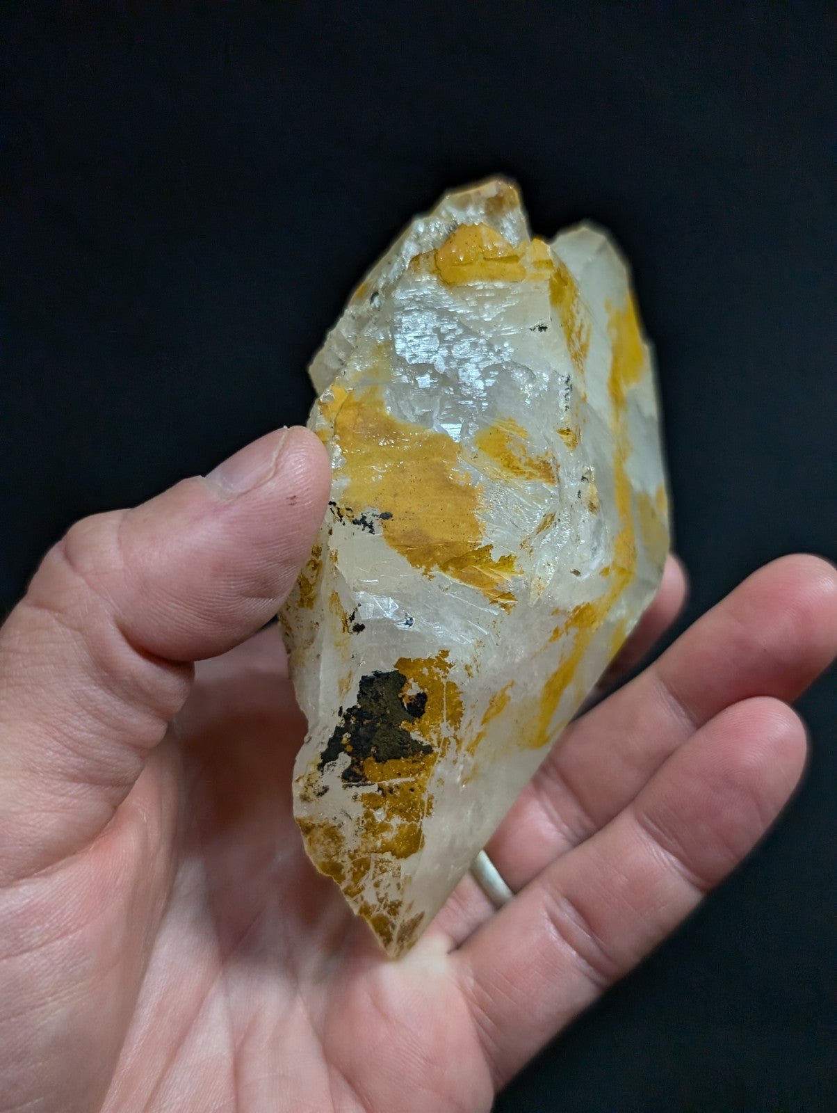 A translucent quartz crystal with vibrant yellow inclusions and a small dark green patch, held gently in someone’s hand.