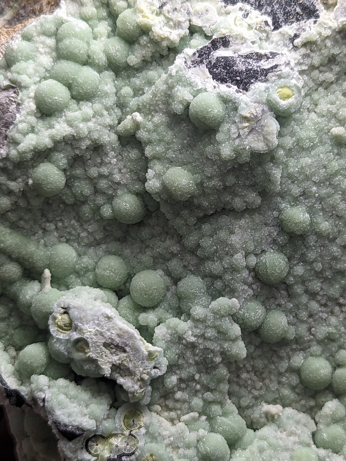 A cluster of pale green, spherical mineral crystals with a textured, crystalline surface.