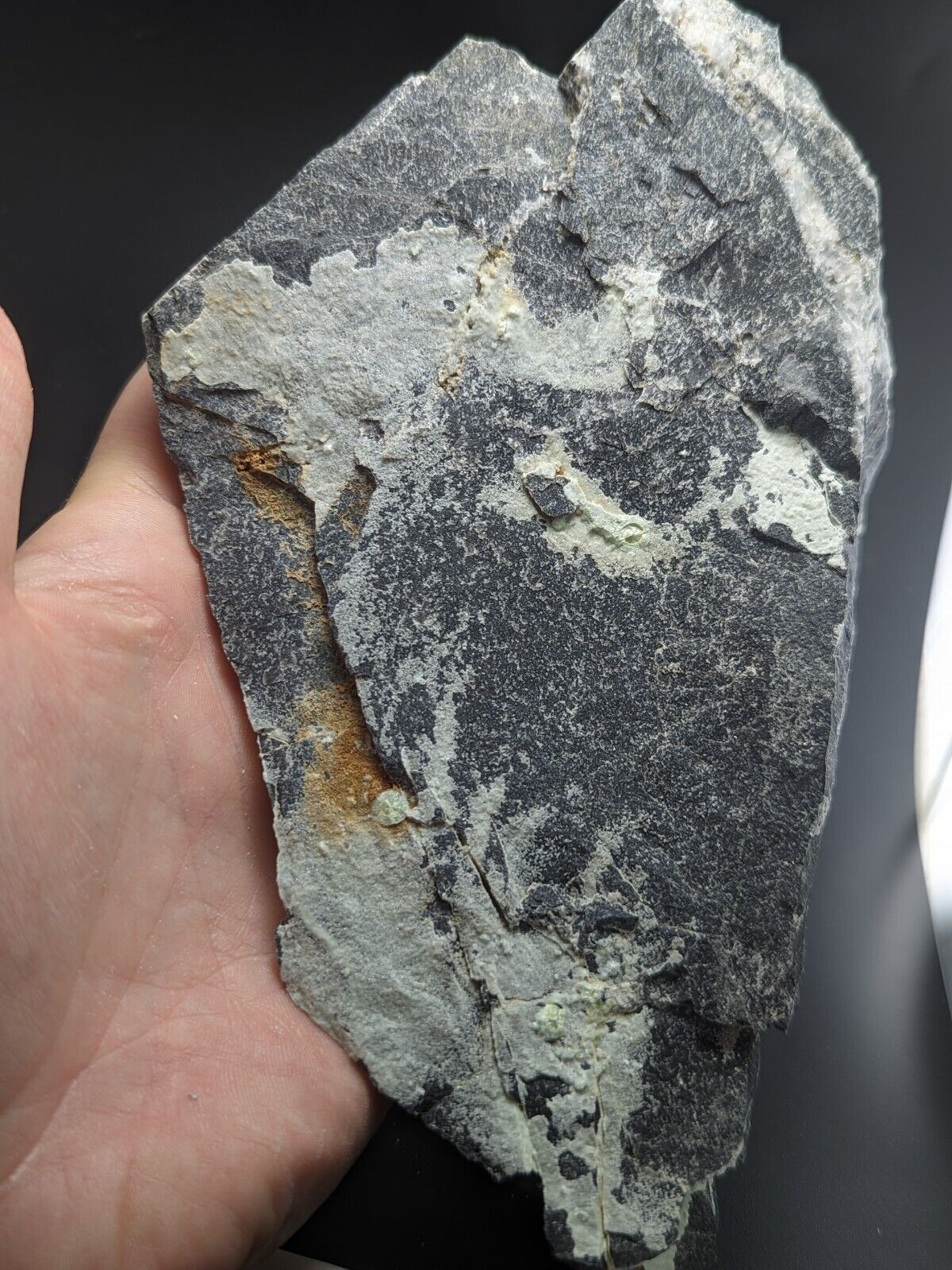 A rugged, irregularly shaped rock with a dark gray base and patches of lighter gray and white mineral veins, accented by subtle orange streaks.