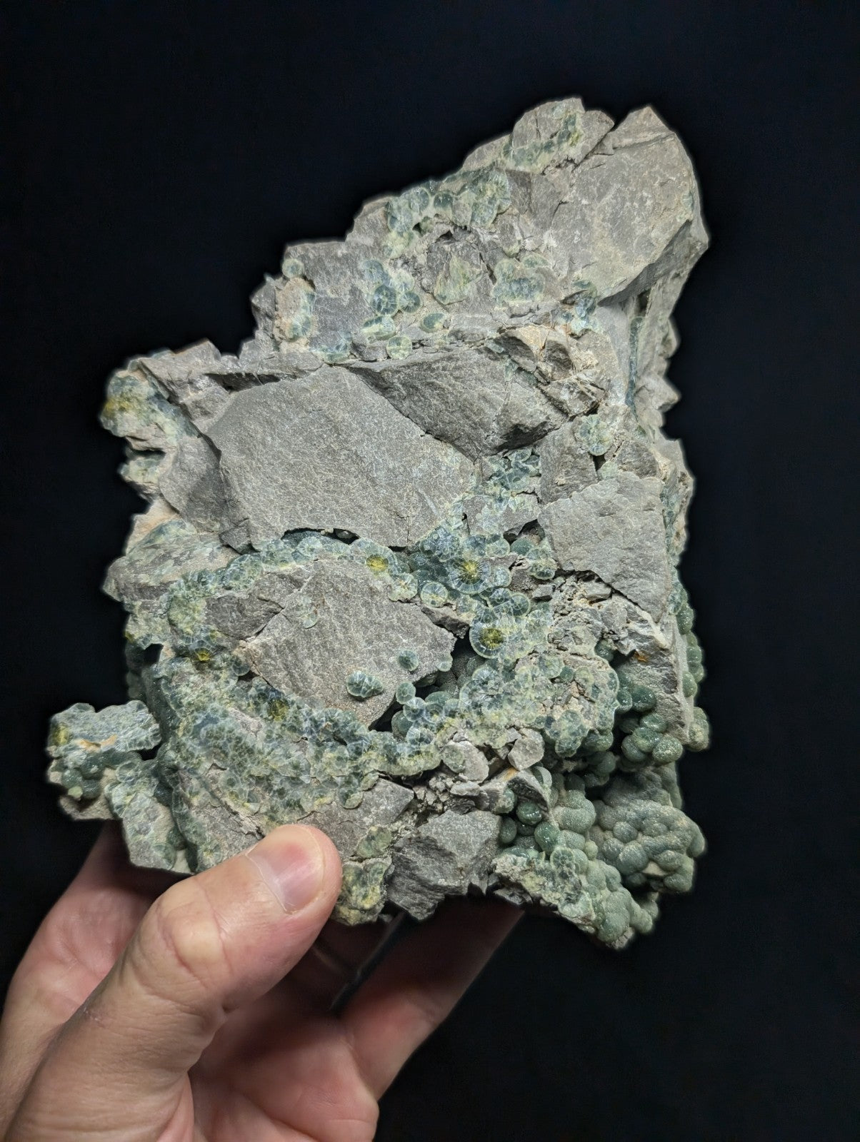 A rough, irregularly shaped mineral specimen with a grayish base and patches of greenish-blue crystalline growths.