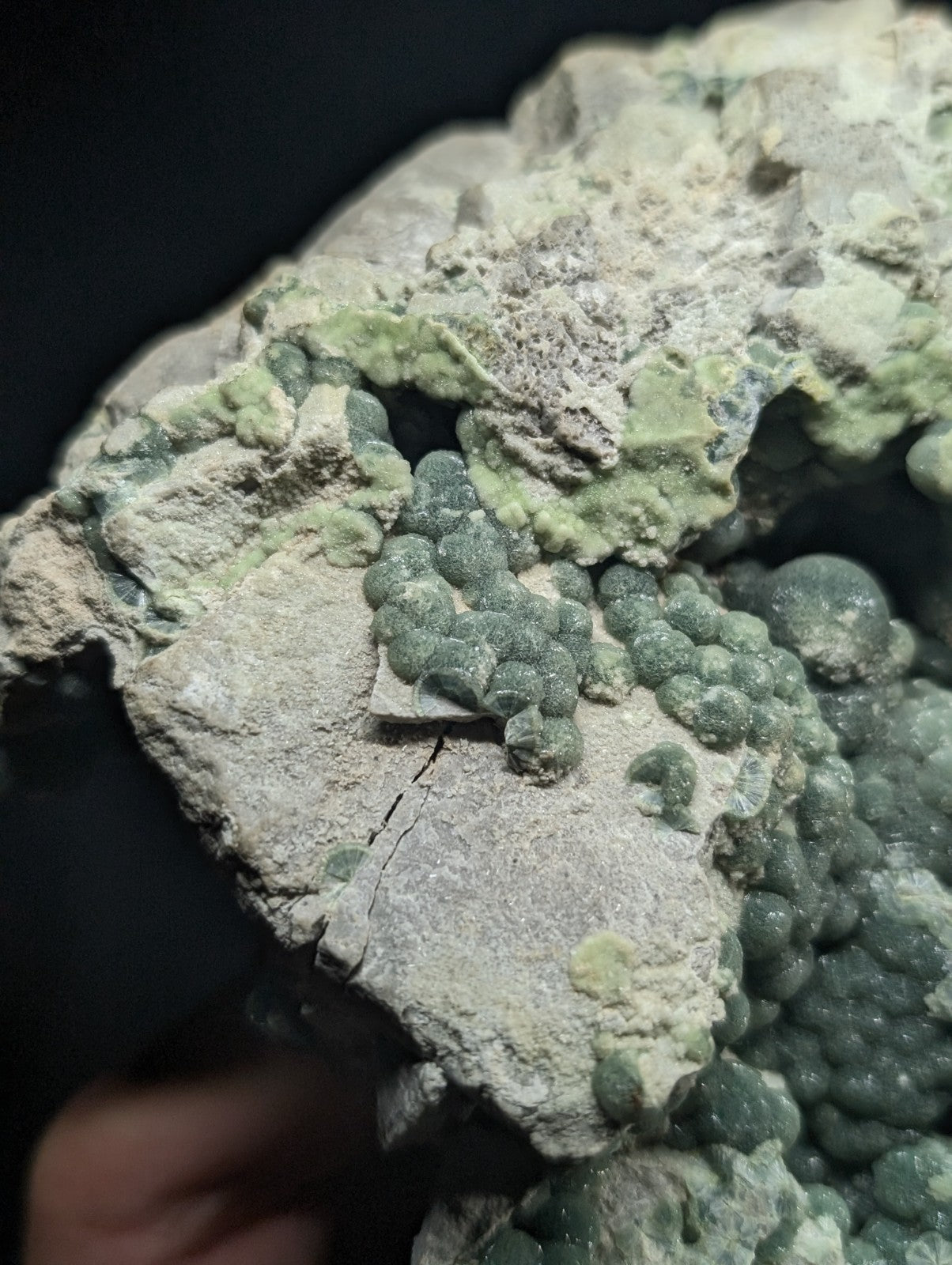 A cluster of green, bead-like minerals growing on a gray rock matrix.