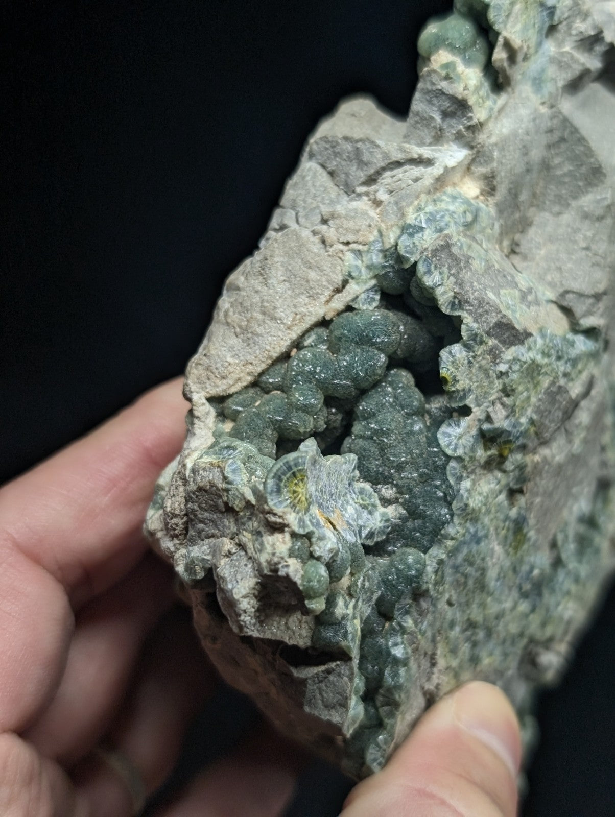 A green, translucent druzy mineral formation embedded in a rough gray rock matrix.