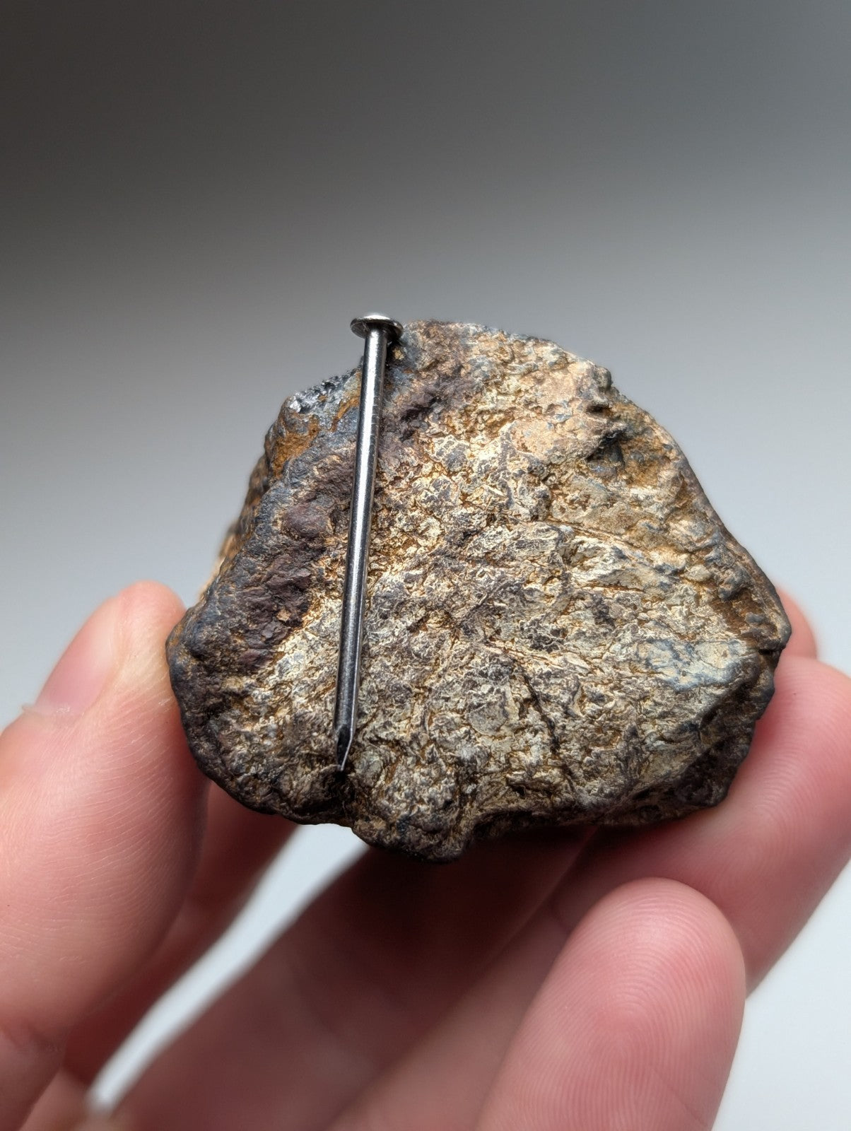 A rough grayish-brown magnetite lodestone with a metallic nail through its center from magnet cove Arkansas