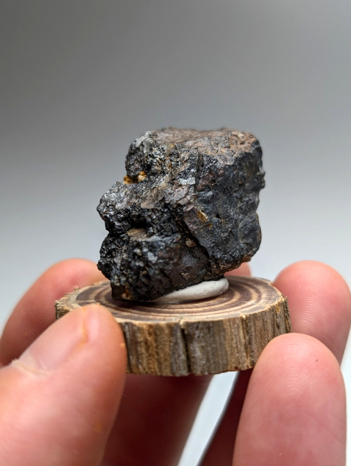 A dark rough-textured magnetite meteorite with metallic sheen on a circular wooden display stand from Arkansas