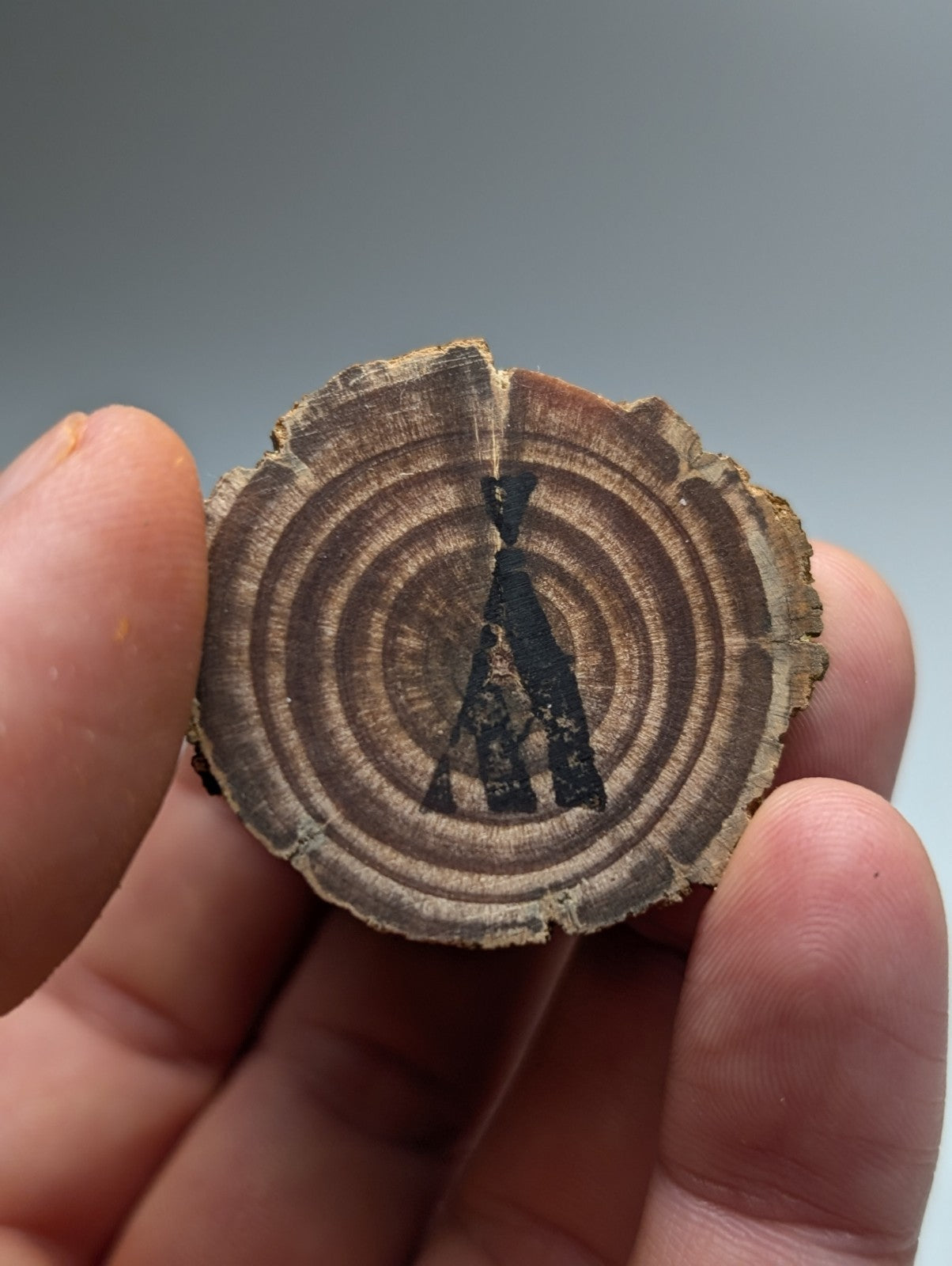 A rustic circular wood slice magnet with black painted teepee silhouette from magnetite magnet cove arkansas on wood stand
