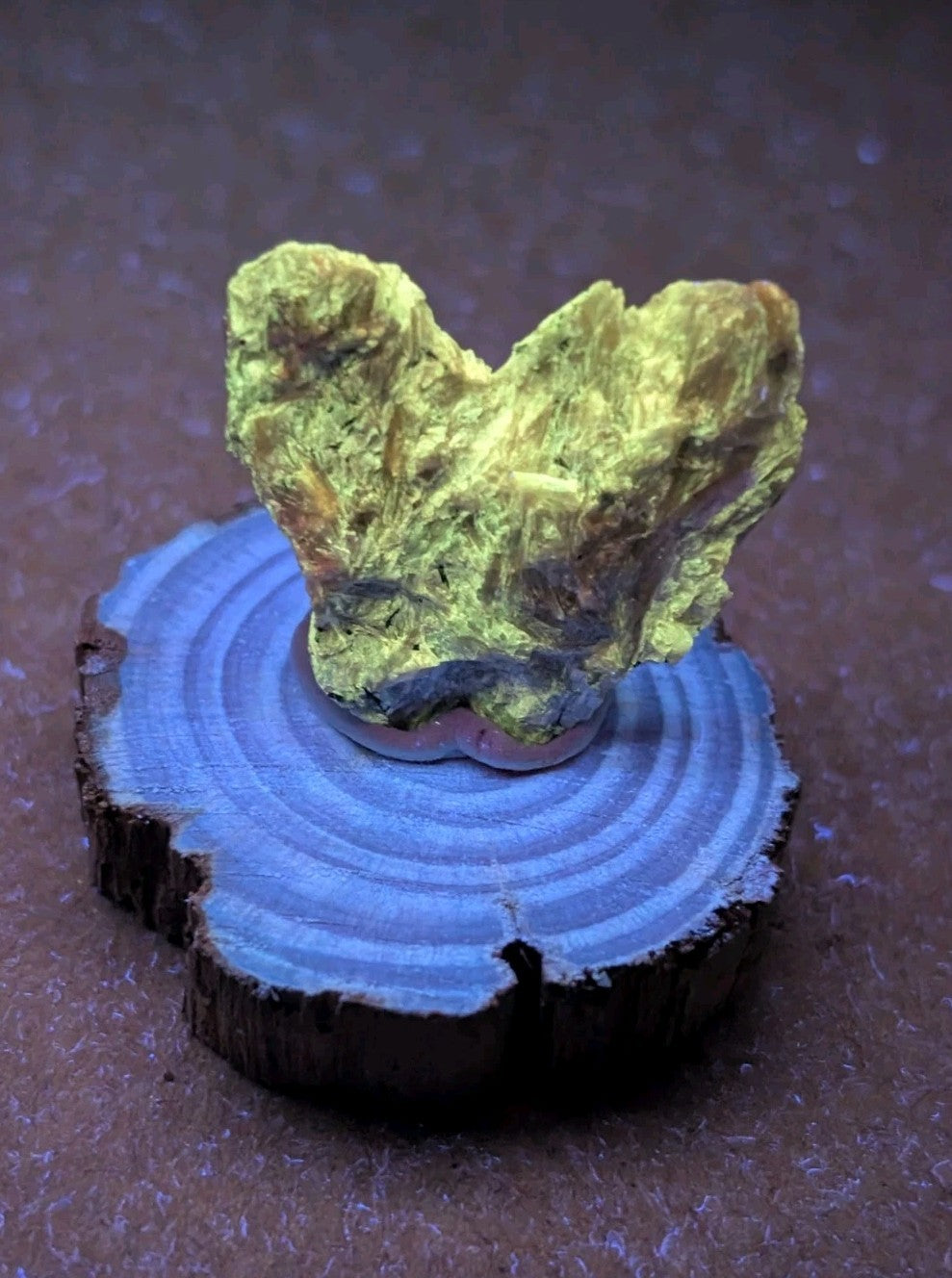 A vibrant, naturally occurring yellow-green mineral specimen with a rough, textured surface and hints of brownish tones, displayed on a circular wooden base.
