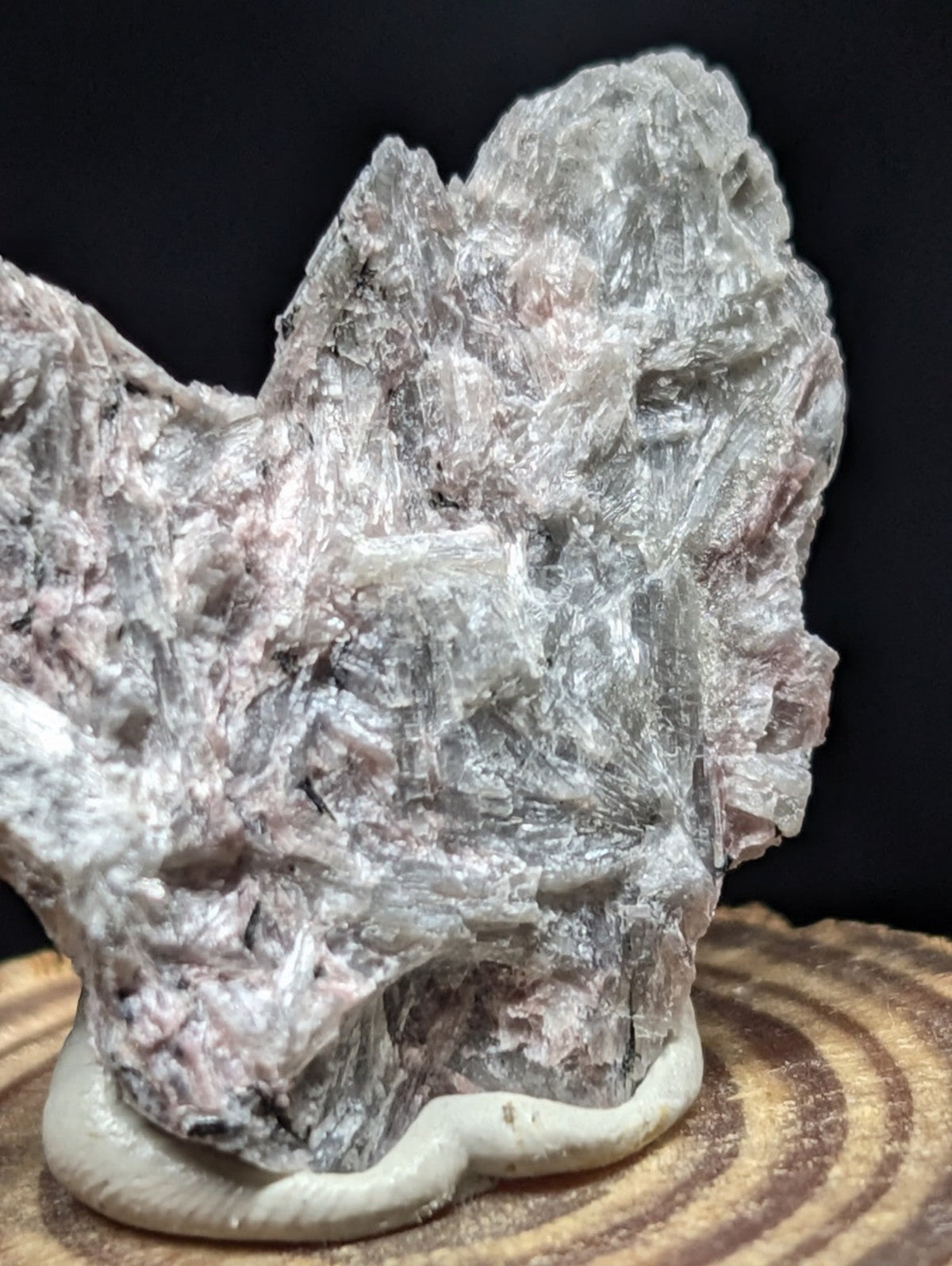 A rugged, translucent gray and pink mineral specimen with crystalline textures rests on a smooth white base.